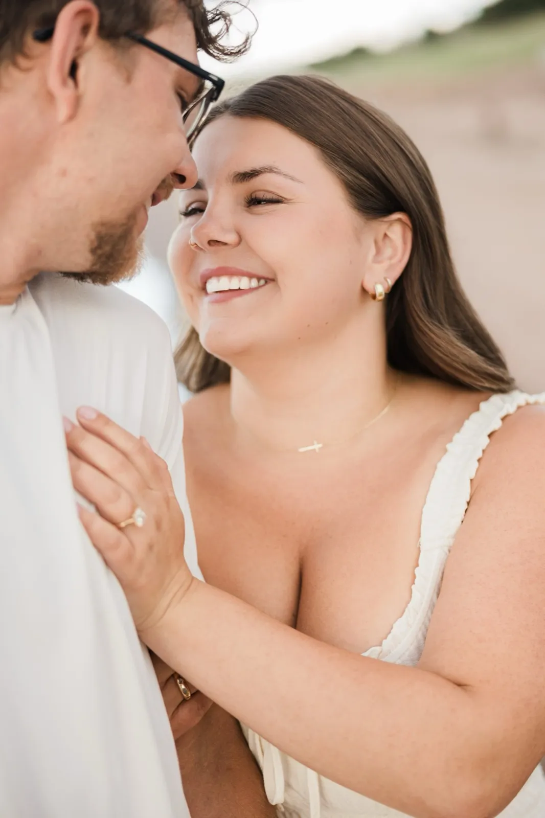 Jacklyn beams up at Reeden with her ring hand on his chest in a close portrait on the Lake Superior shore — Tim Larsen Photography