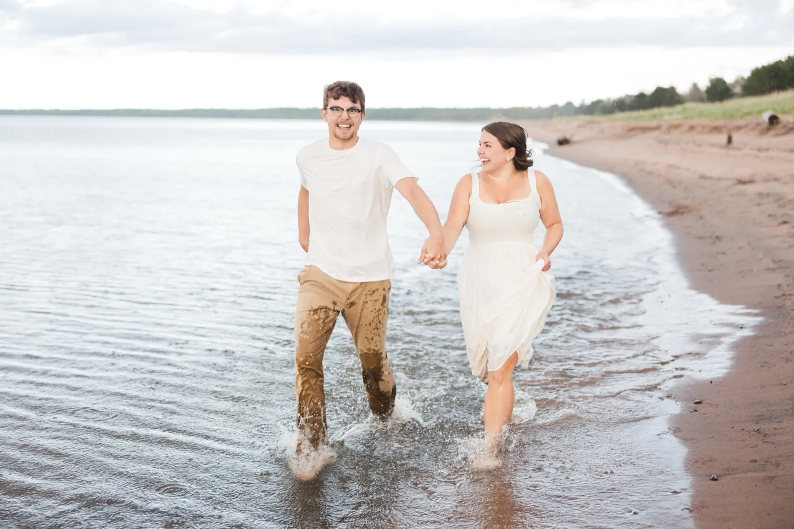 Reeden and Jacklyn run splashing hand in hand through the Lake Superior shallows, both laughing — Tim Larsen Photography