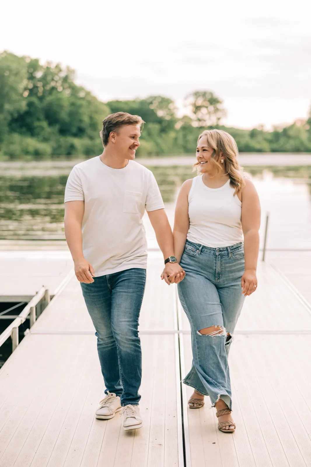 Abby and Anthony walk hand in hand along the Lake Auburn dock, the lake behind them — Tim Larsen Photography
