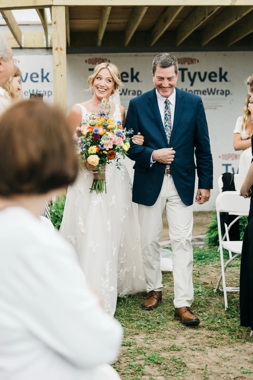 The bride beams while walking down the aisle on her father's arm, holding a vibrant wildflower bouquet as guests look on. — Tim Larsen Photography, Brainerd Lakes MN