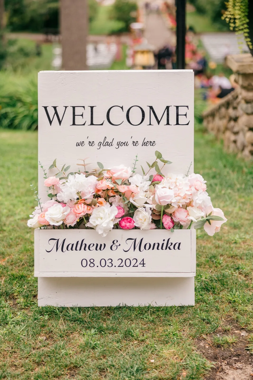 White wooden welcome sign with pink florals on the lawn outside the Grand View Lodge ceremony — Tim Larsen Photography, Brainerd Lakes MN
