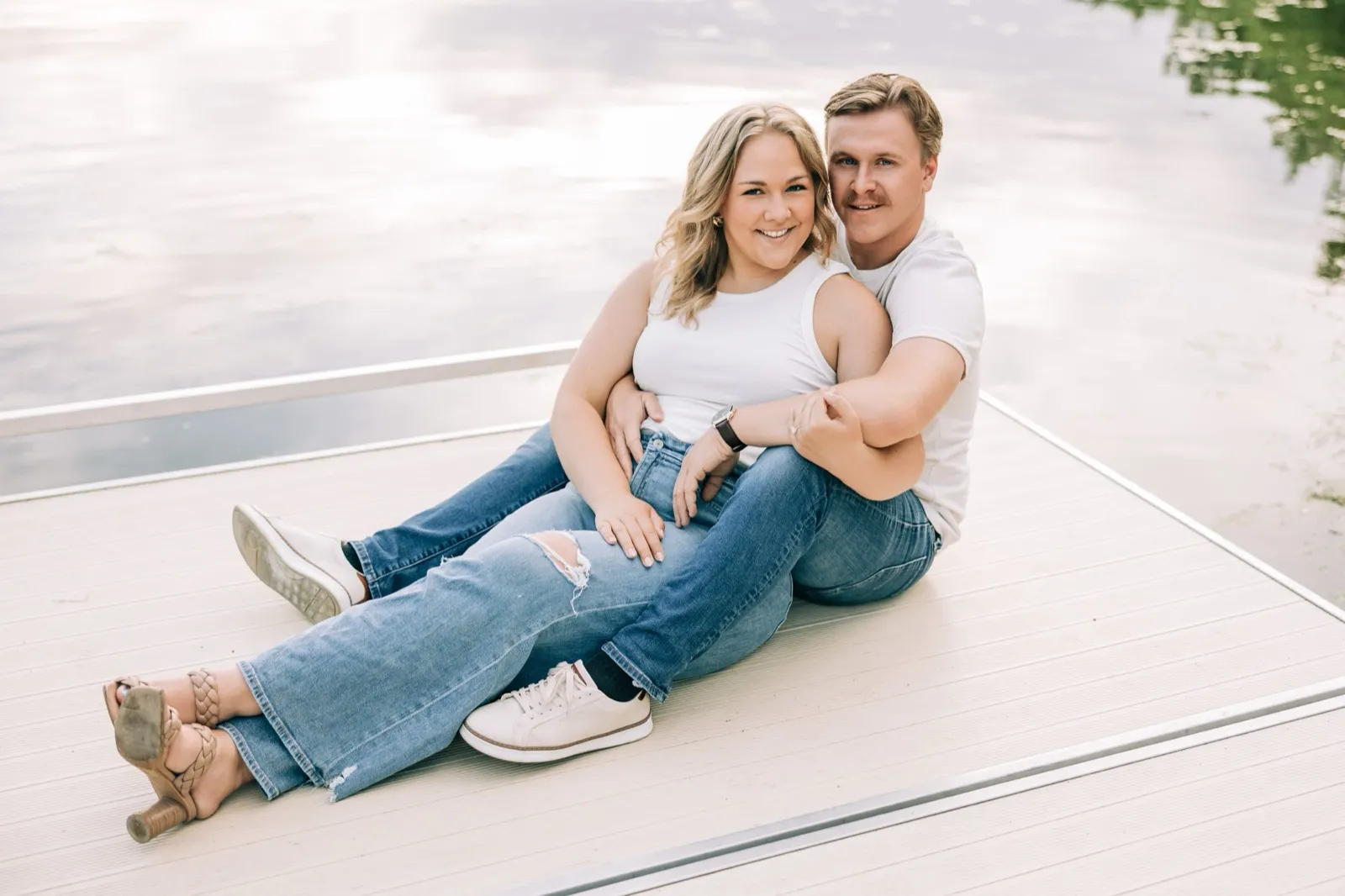 Abby and Anthony lean back on the dock and smile at the camera, the lake behind them — Tim Larsen Photography