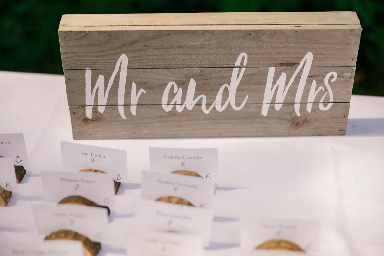 A rustic wooden Mr and Mrs sign sits above escort cards held in birch wood slice stands on a white linen table. — Tim Larsen Photography, Brainerd Lakes MN