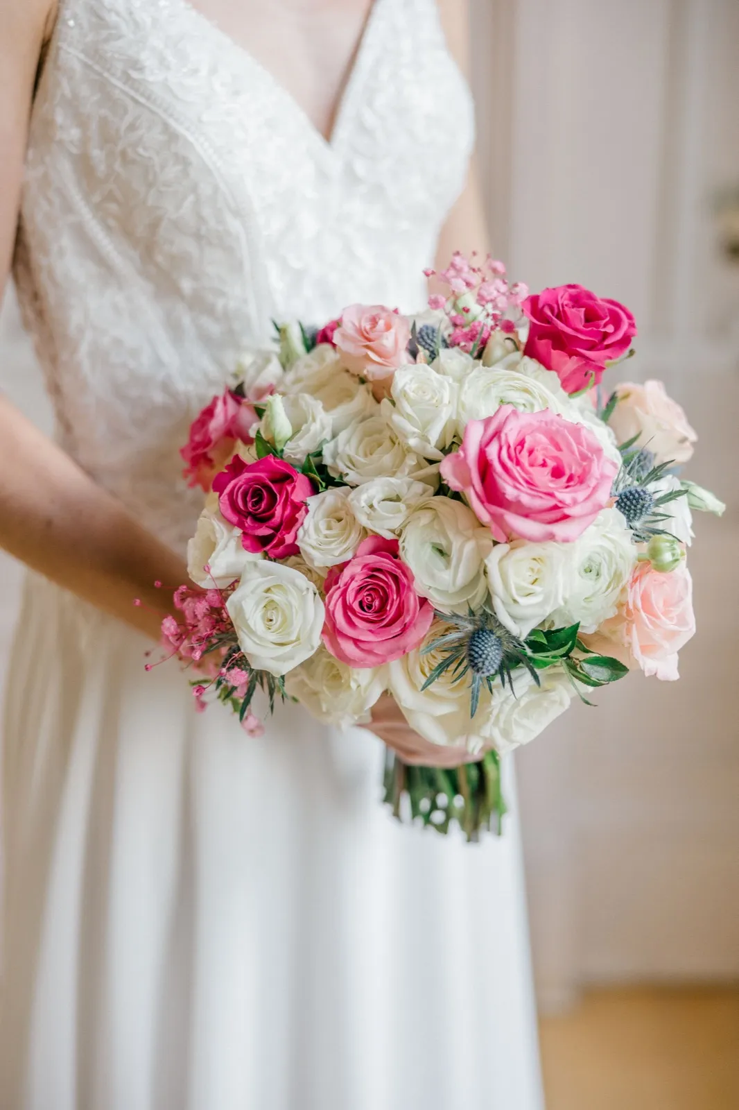 The bride holds a bouquet of pink and white roses, ranunculus, and blue thistle against her white lace gown. — Tim Larsen Photography, Minneapolis MN