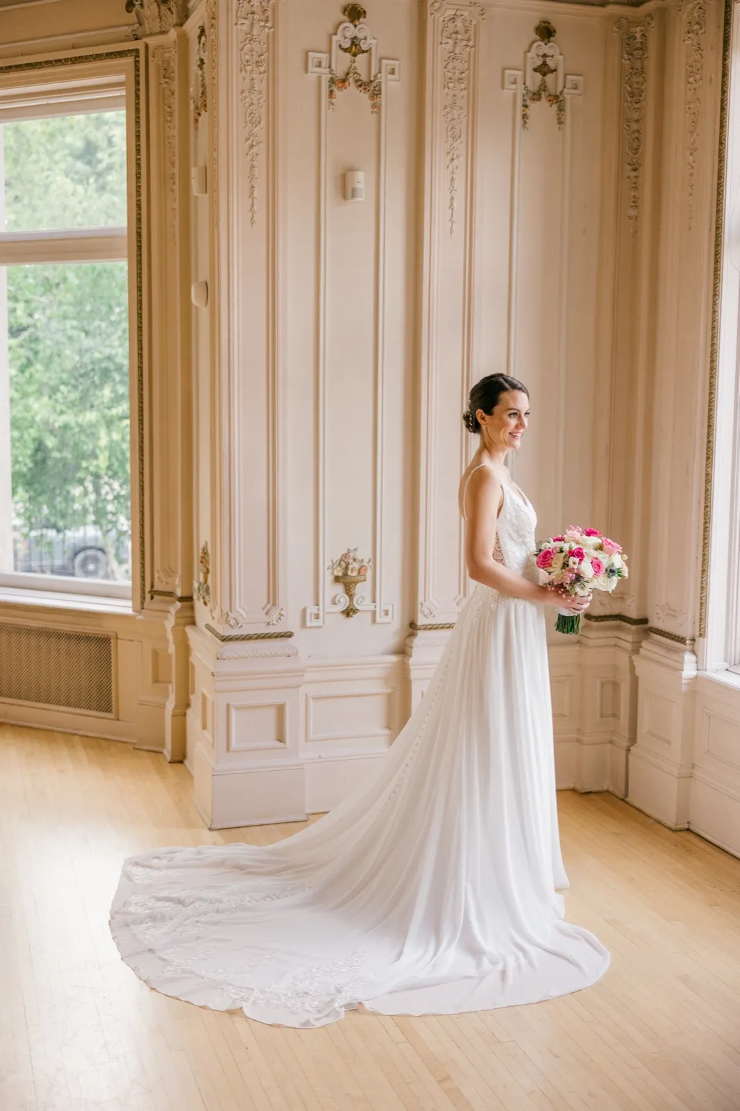 The bride stands in a full-length gown holding a pink and white bouquet inside an ornately paneled room at the American Swedish Institute, her train fanned out across the hardwood floor. — Tim Larsen Photography, Minneapolis MN