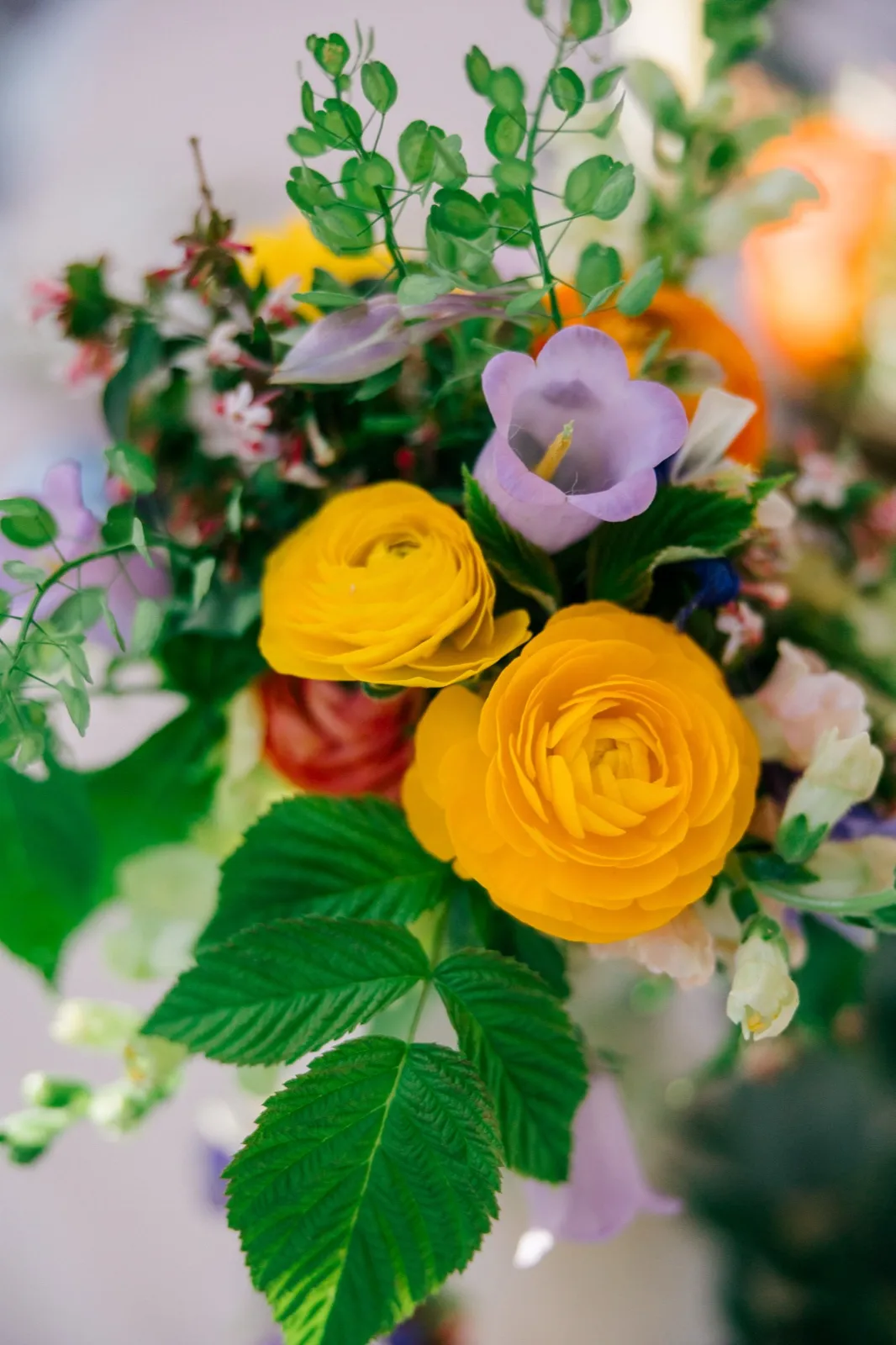 Close-up of a bridal bouquet featuring yellow ranunculus, lavender bellflowers, peach roses, and trailing greenery — Tim Larsen Photography, Brainerd Lakes MN