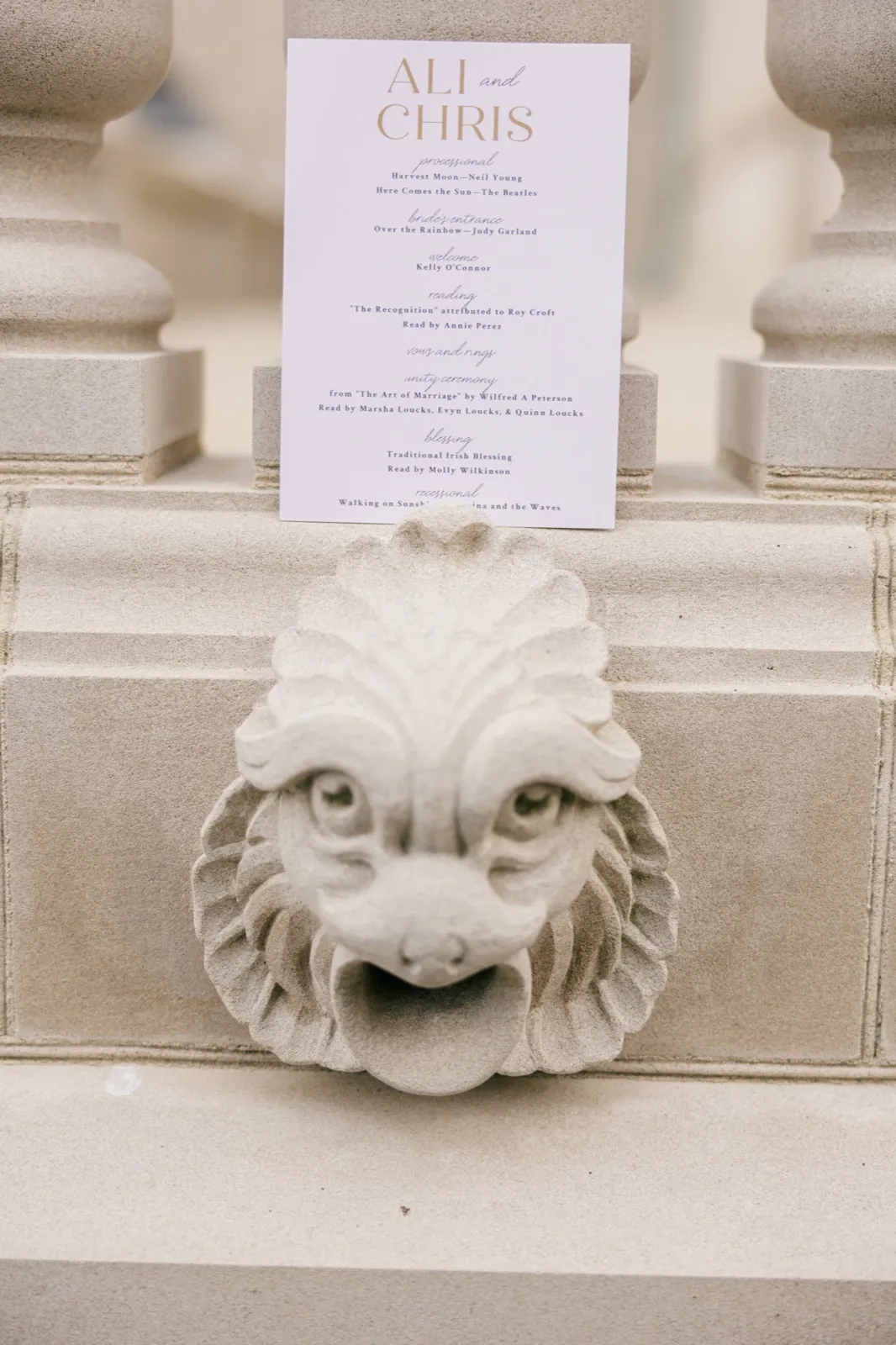A wedding ceremony program for Ali and Chris rests against stone balusters above a carved lion's-head sculpture on the steps of the American Swedish Institute. — Tim Larsen Photography, Minneapolis MN