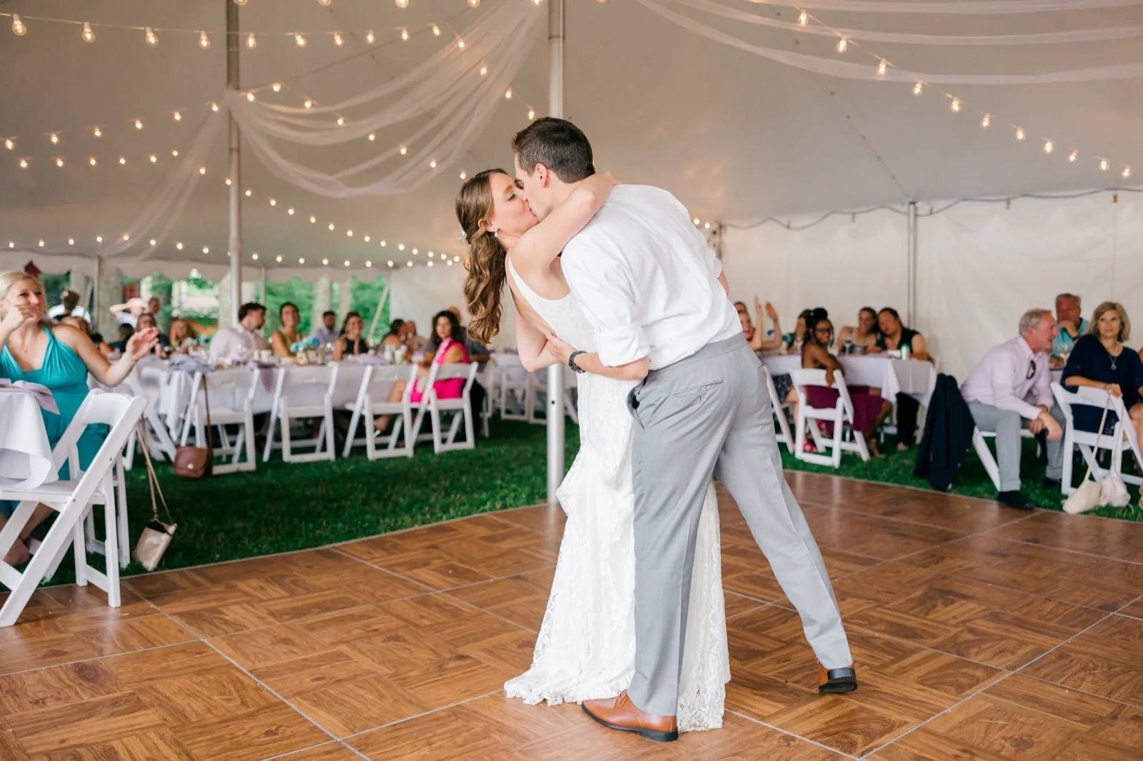 The groom dips the bride into a kiss on a parquet dance floor under a string-lit tent while seated guests watch from long tables. — Tim Larsen Photography, Brainerd Lakes MN