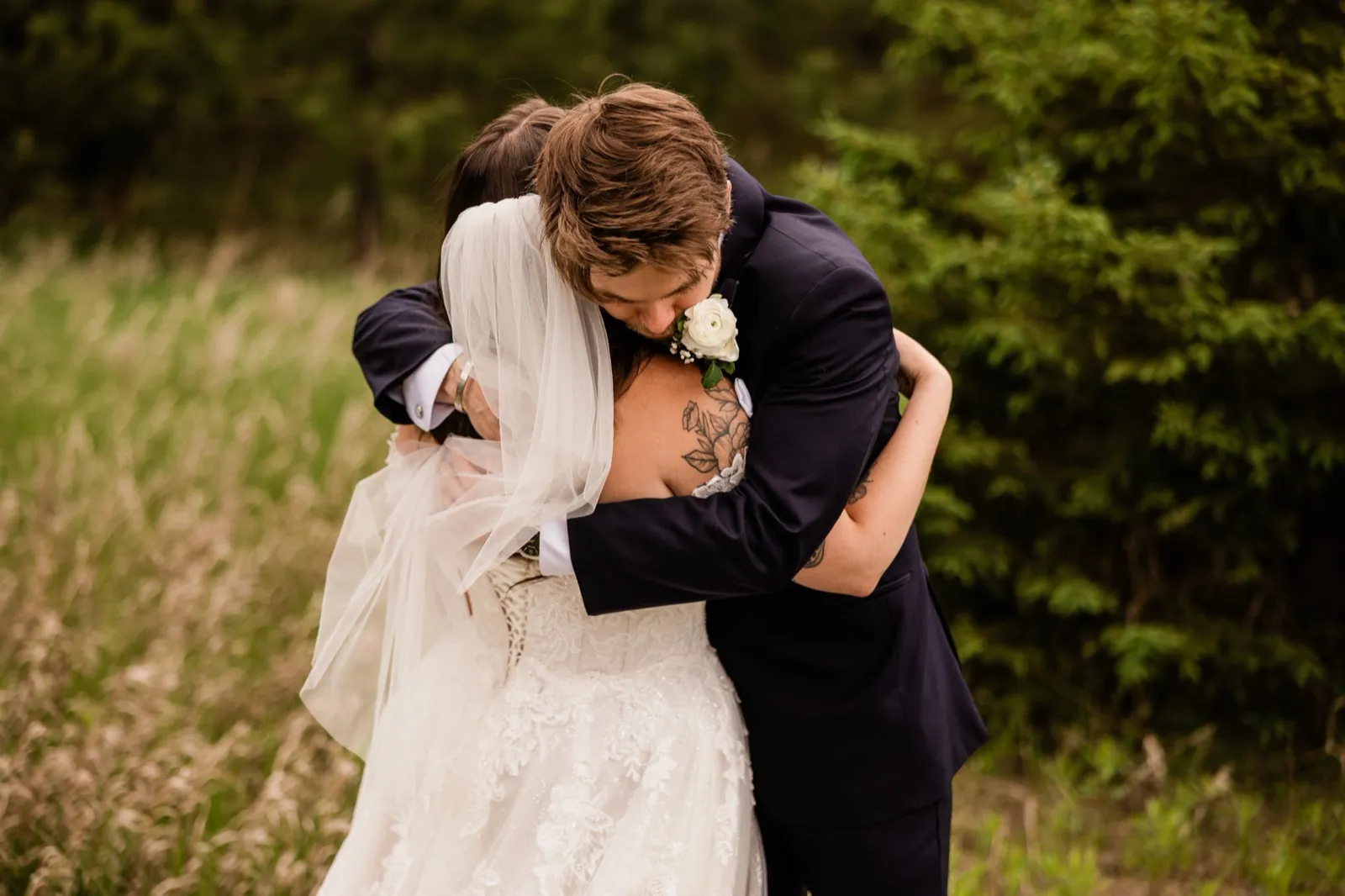 A bride and groom hold each other close in a meadow during their first look, the groom's face pressed into her shoulder — the calm moment a buffer protects — Tim Larsen Photography, Brainerd Lakes MN