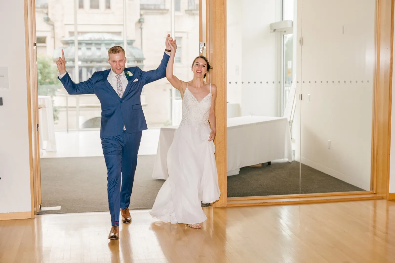 The bride and groom raise their joined hands in triumph as they enter the reception space through a doorway, with the historic American Swedish Institute mansion visible through a window behind them. — Tim Larsen Photography, Minneapolis MN