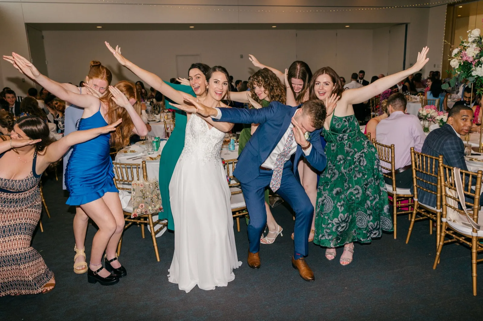 The bride, groom, and a group of friends strike a coordinated arms-out pose on the reception floor, all grinning at the camera. — Tim Larsen Photography, Minneapolis MN