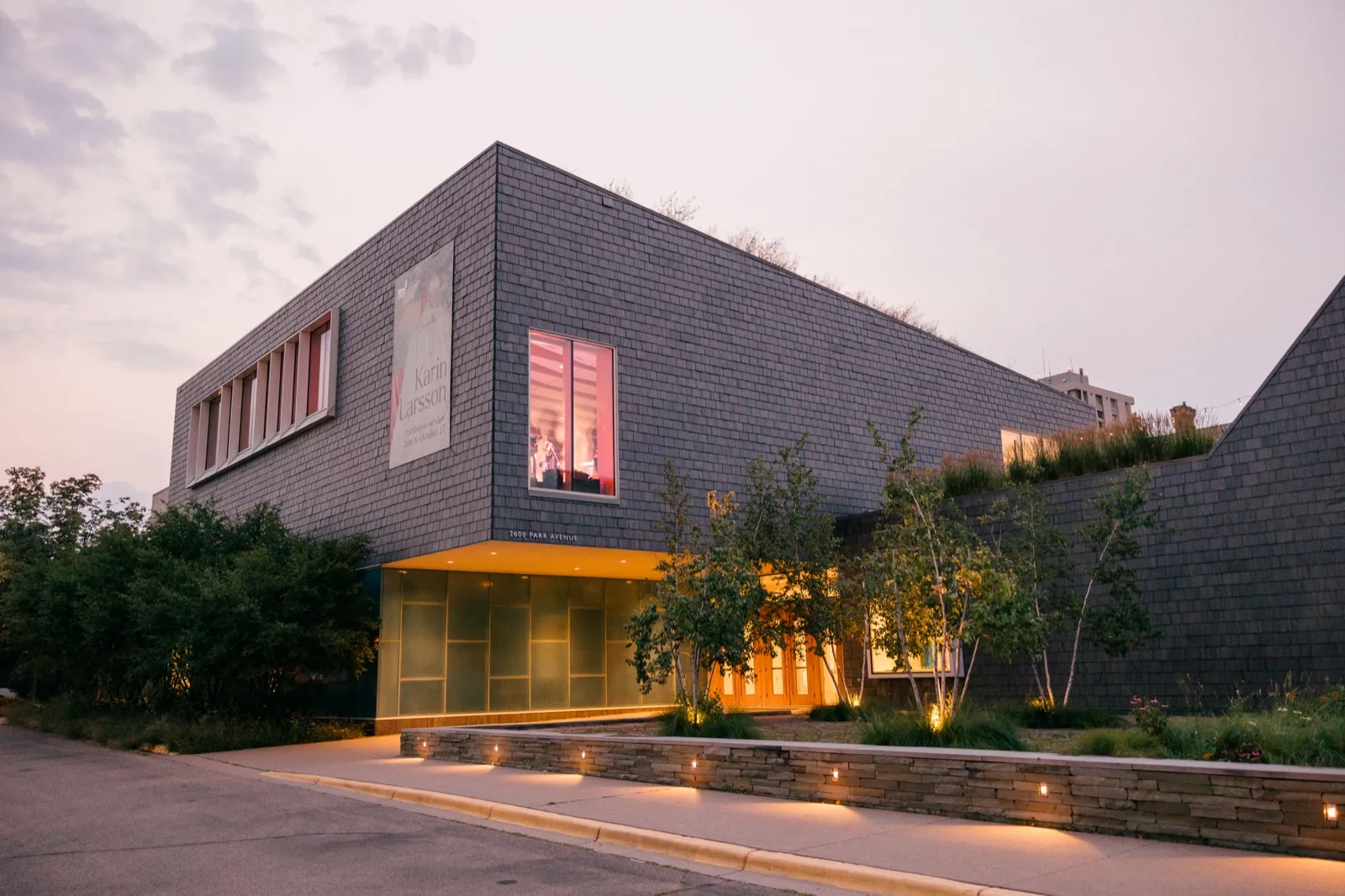 The slate-clad exterior of the American Swedish Institute's Nelson Cultural Center at dusk, with warm light spilling from the entrance and a pastel sky overhead. — Tim Larsen Photography, Minneapolis MN