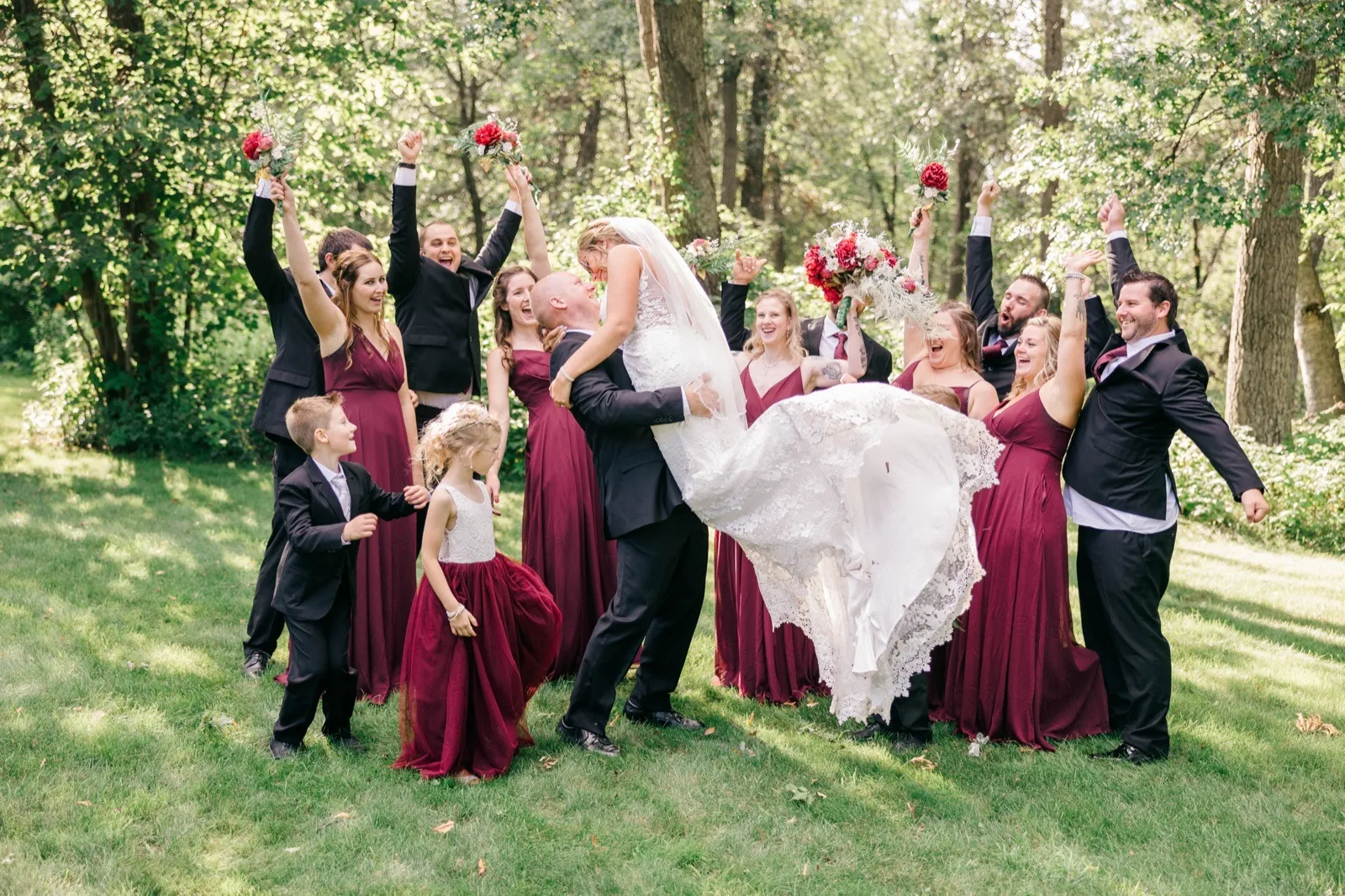 Jesse dips Kim for a kiss while their bridal party cheers with raised bouquets and arms on a sunlit lawn at Whitefish Lodge — Tim Larsen Photography, Brainerd Lakes MN