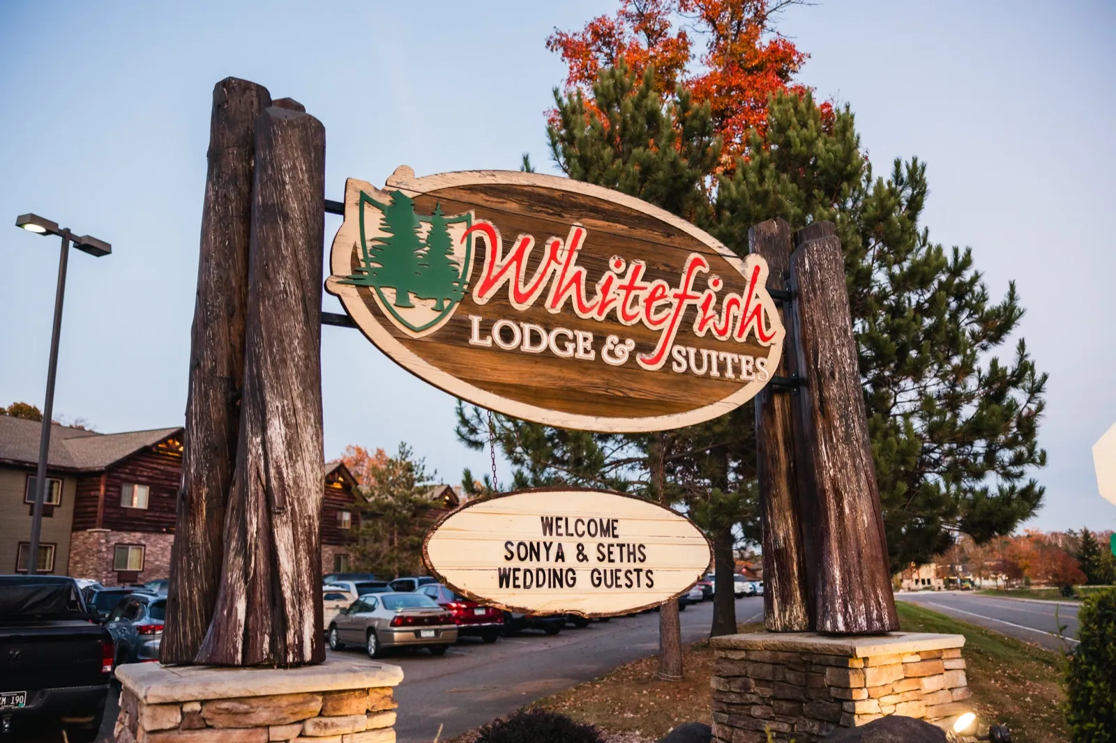 The carved wooden Whitefish Lodge & Suites entrance sign welcomes wedding guests beneath autumn pines at dusk — Tim Larsen Photography, Brainerd Lakes MN