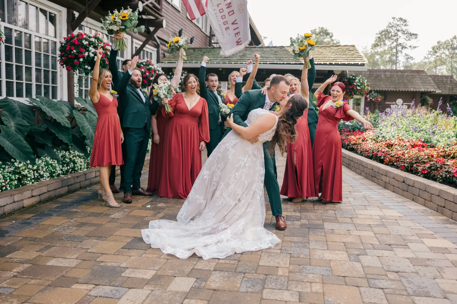 Eric dips Chelsea into a kiss on a paver walkway while the bridal party cheers with raised bouquets beneath the Grand View Lodge flag — Tim Larsen Photography, Brainerd Lakes MN