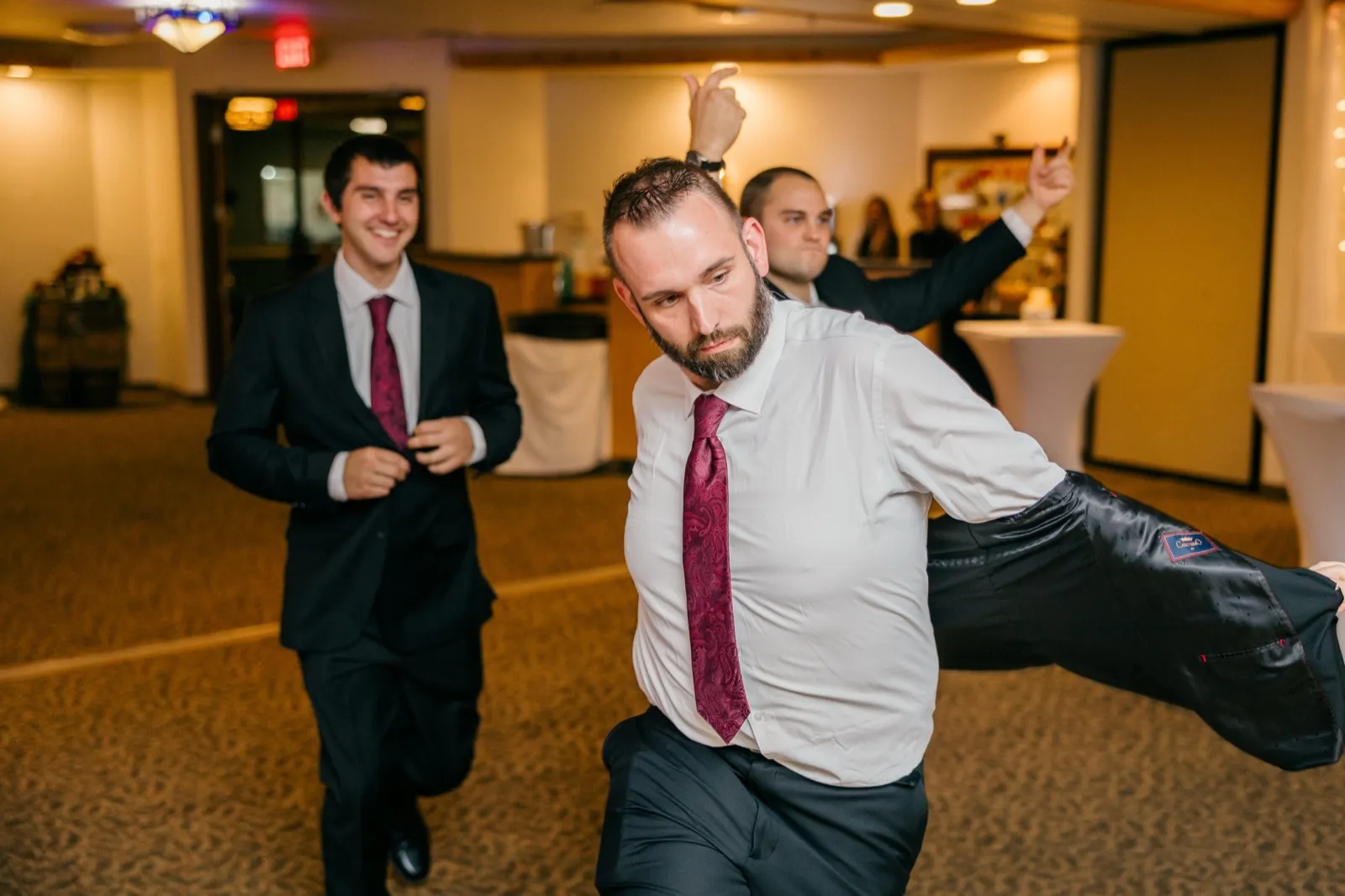 A groomsman swings his suit jacket out to one side mid-dance while another laughs and dances behind him on the reception dance floor — Tim Larsen Photography, Brainerd Lakes MN