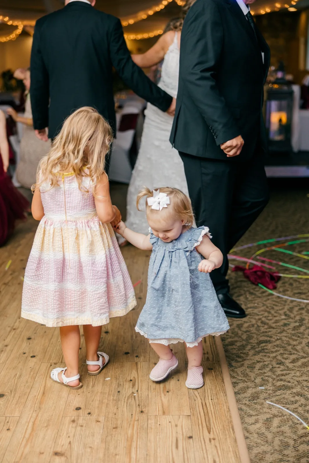 Two small girls in pastel dresses stand on the dance floor holding hands with the bride and groom — Tim Larsen Photography, Brainerd Lakes MN
