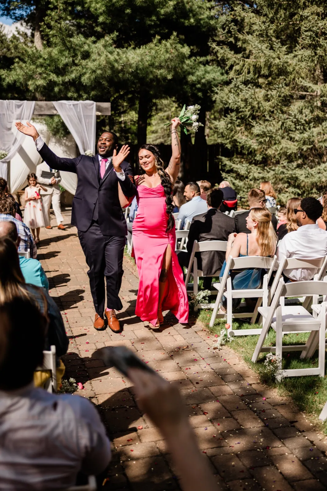 Bridesmaid and groomsman cheering with arms raised during the bridal party recessional