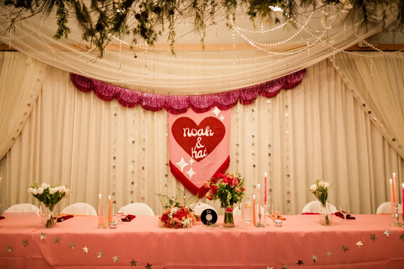 Sweetheart table with pink banner, draped fabric, star garlands and tapers at the Pine Peaks reception