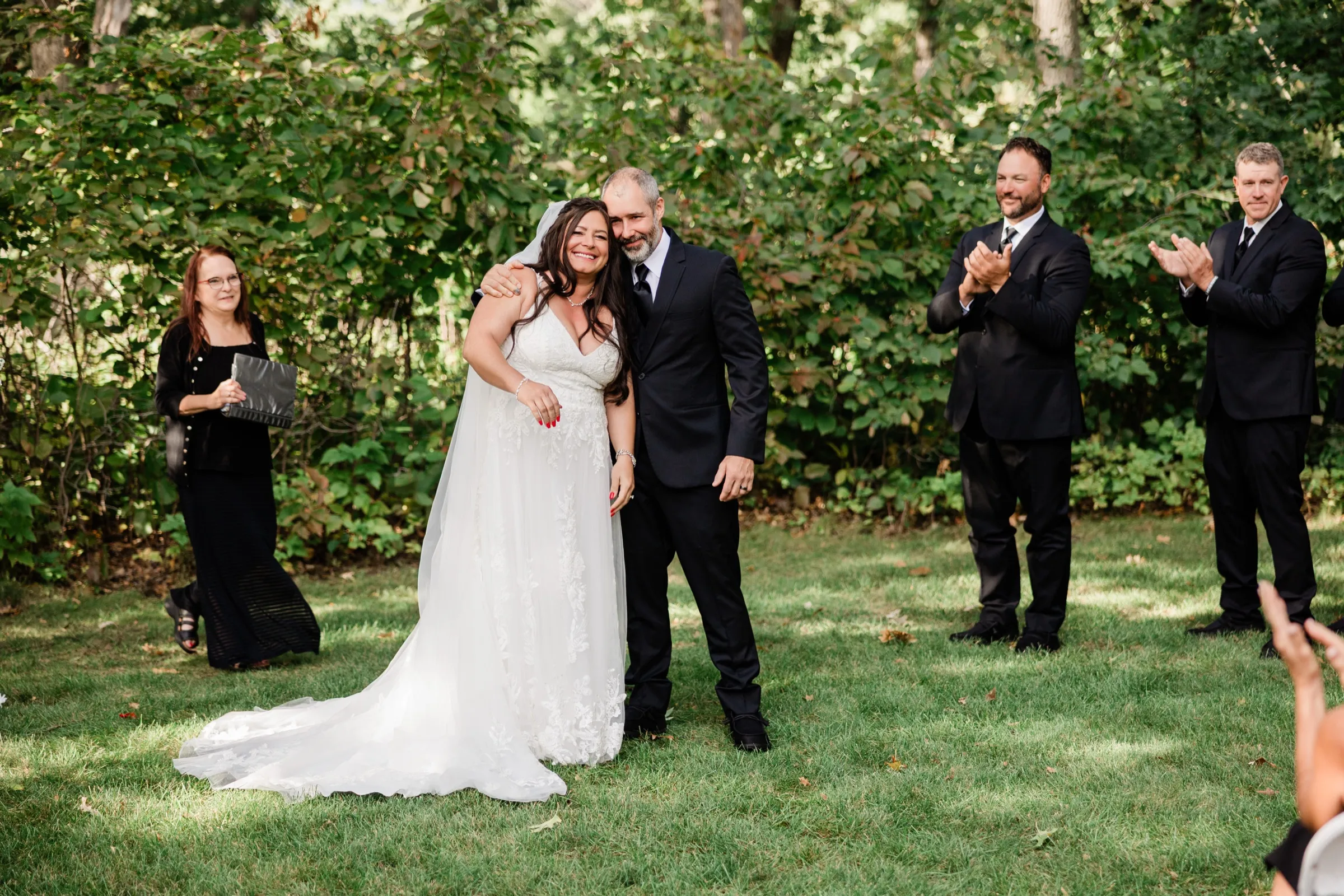 Don wraps an arm around Amber as she beams toward the guests just after the kiss, while groomsmen clap and the officiant steps aside. — Tim Larsen Photography, Brainerd Lakes MN