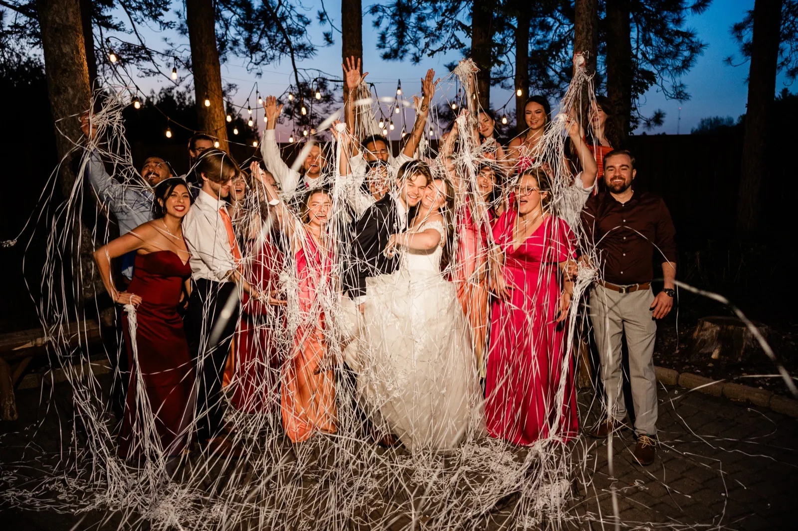 Streamer send-off with the full wedding party under the string lights at blue hour