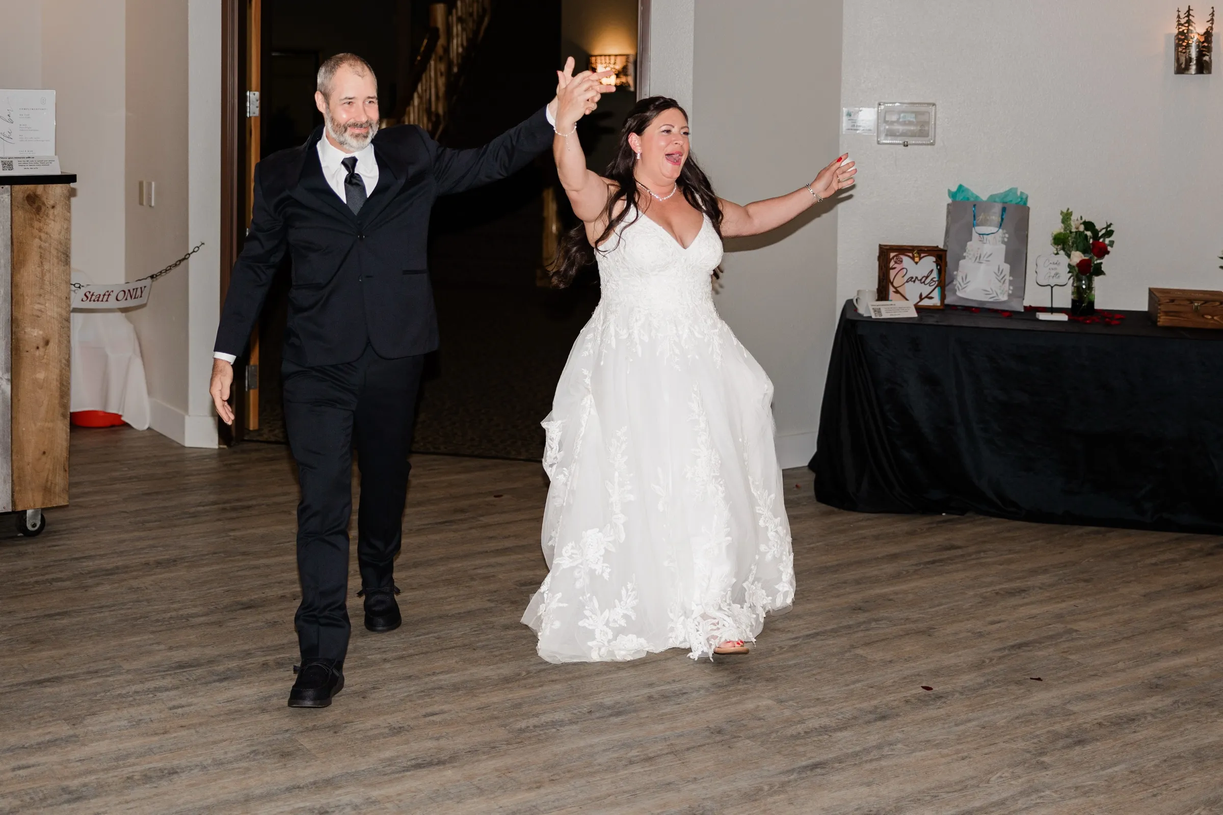 Amber and Don walk into the reception hand in hand with their arms raised, Amber cheering, past a card and gift table. — Tim Larsen Photography, Brainerd Lakes MN