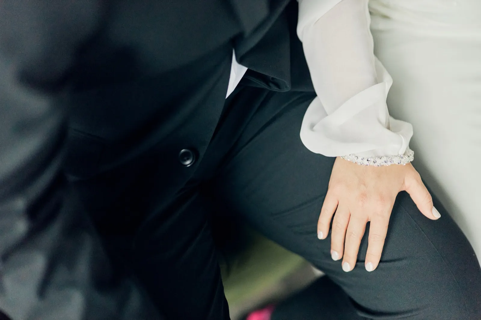The bride's hand wearing a beaded bracelet rests on the groom's knee as they sit beside each other in formal attire. — Tim Larsen Photography, Brainerd Lakes MN