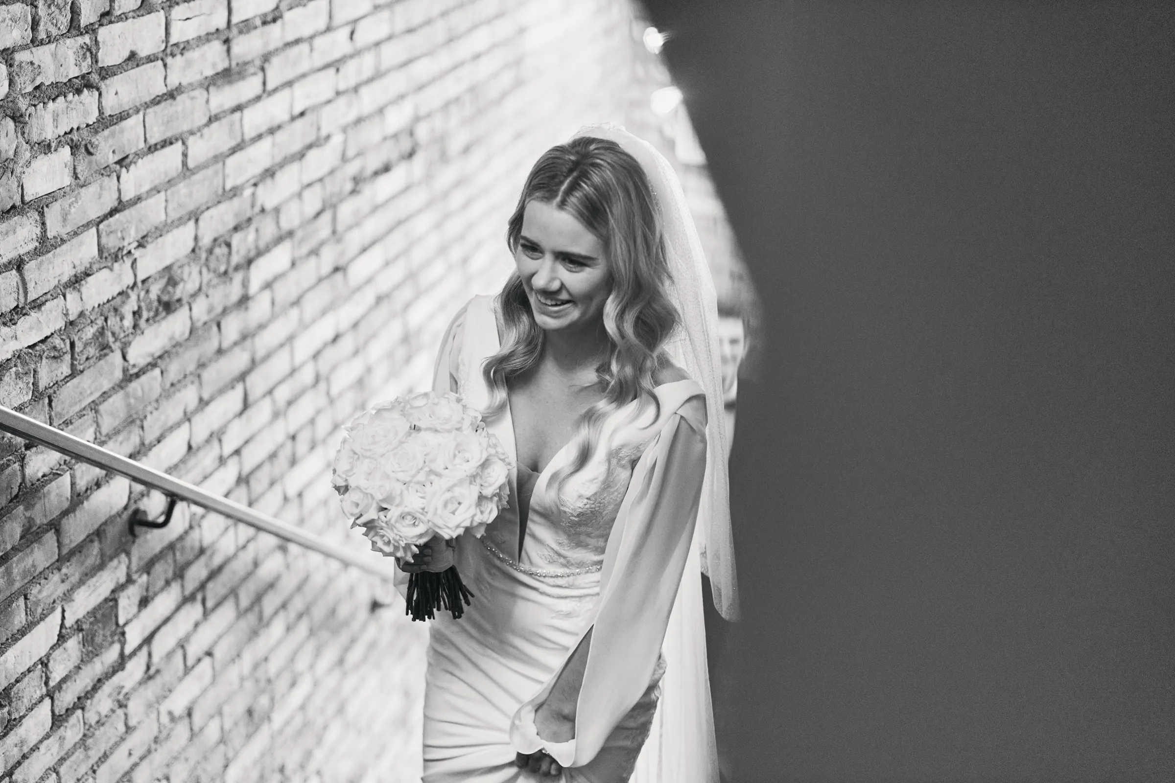Madeline smiles as she walks up a brick stairwell holding her bouquet, her veil trailing behind her — Tim Larsen Photography, Brainerd Lakes MN