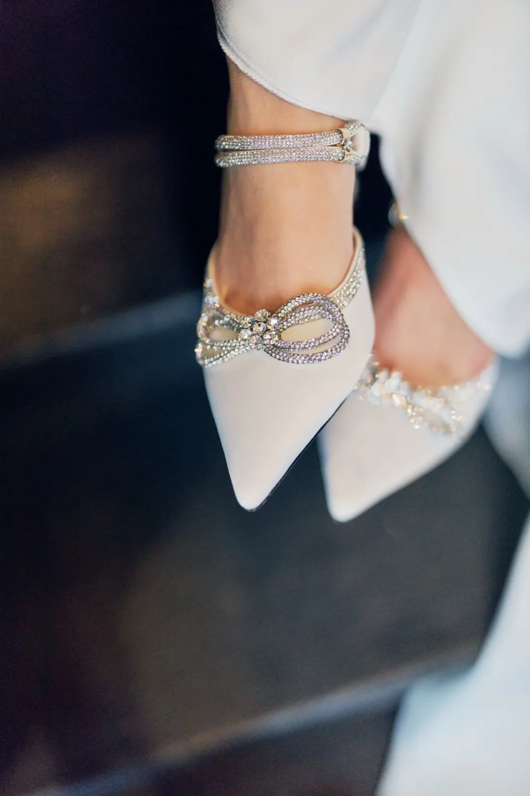 A close-up of the bride's feet wearing white pointed-toe heels with crystal bow embellishments and rhinestone ankle straps. — Tim Larsen Photography, Brainerd Lakes MN