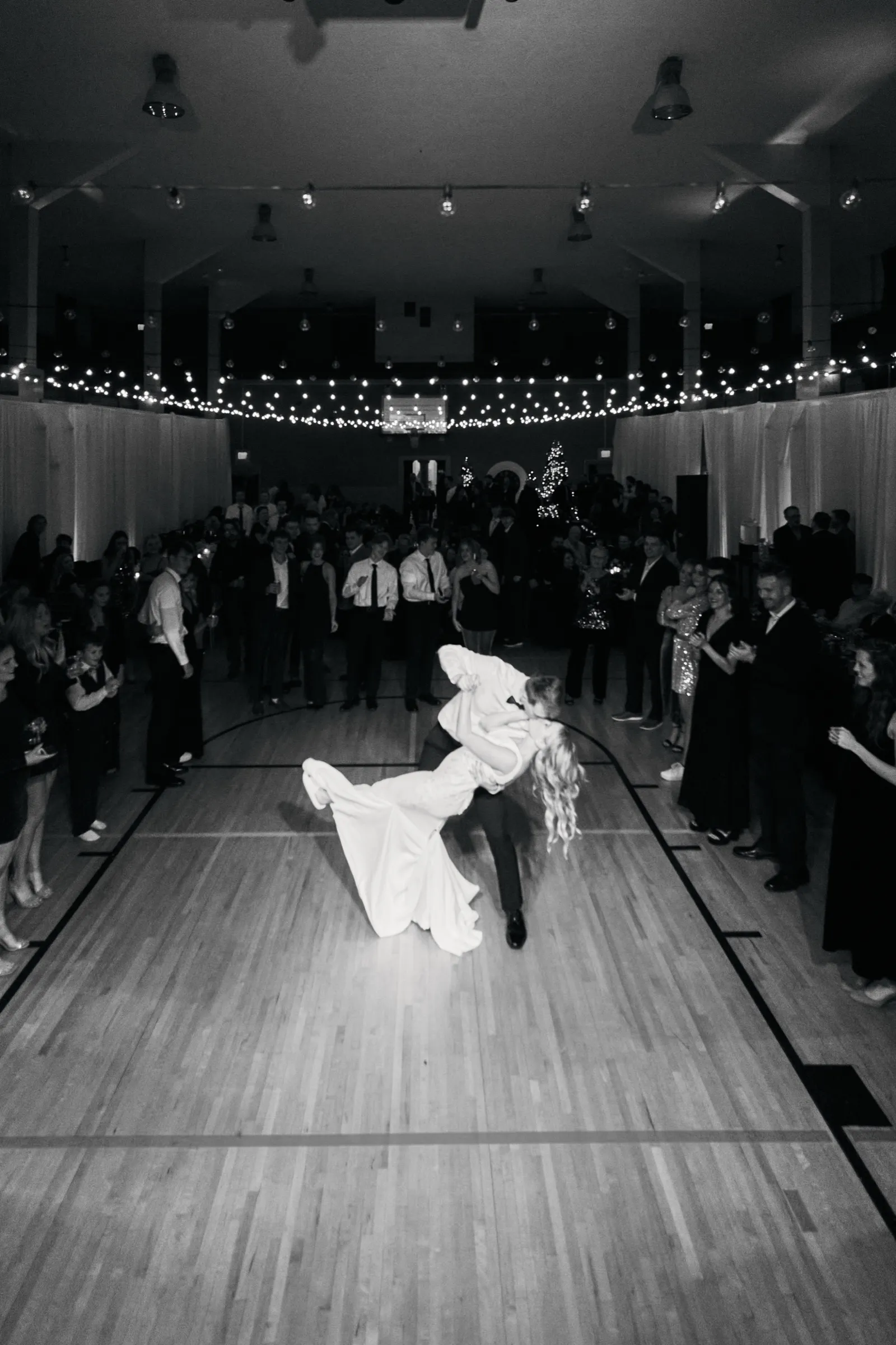 Sam dips Madeline at the center of a string-light-canopied dance floor in the Deerwood Auditorium gymnasium while guests ring the perimeter watching — Tim Larsen Photography, Brainerd Lakes MN