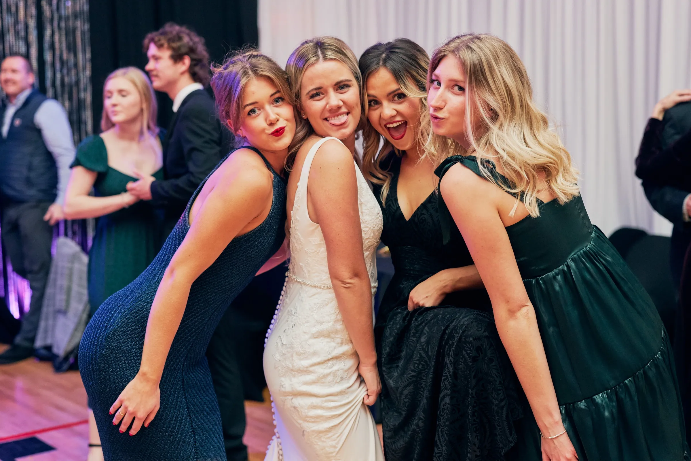 Madeline leans toward the camera with three friends in jewel-toned dresses, all making playful faces on the reception dance floor — Tim Larsen Photography, Brainerd Lakes MN
