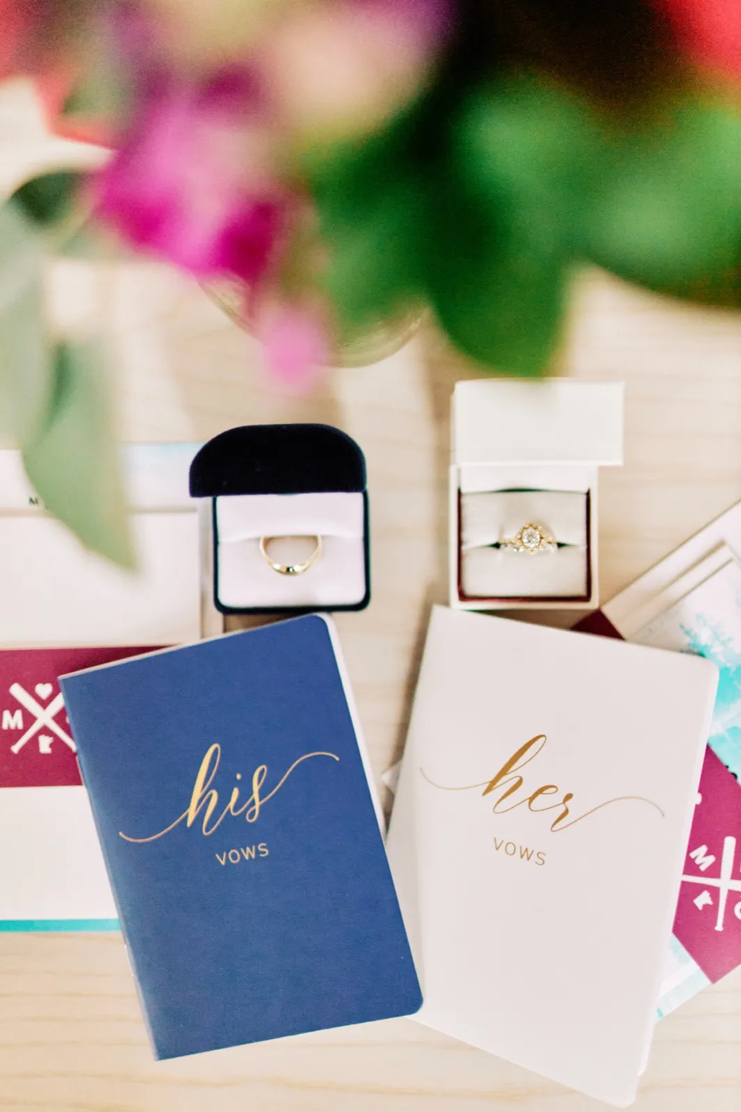 Maggie and Craig's navy and white vow books lie beside their rings and printed monogram, framed by soft pink flowers — Tim Larsen Photography, Brainerd Lakes MN