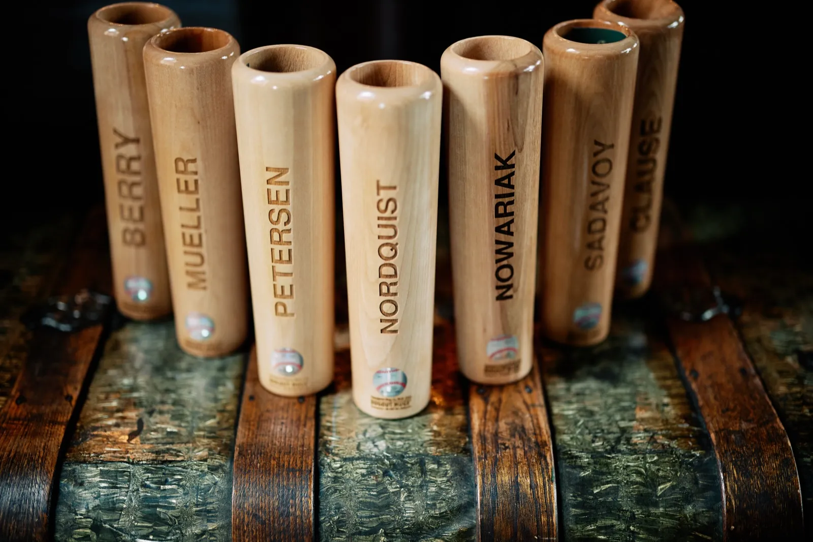 Custom engraved baseball-bat beer glasses lined up on a weathered whiskey barrel, Craig's gifts to his groomsmen — Tim Larsen Photography, Brainerd Lakes MN