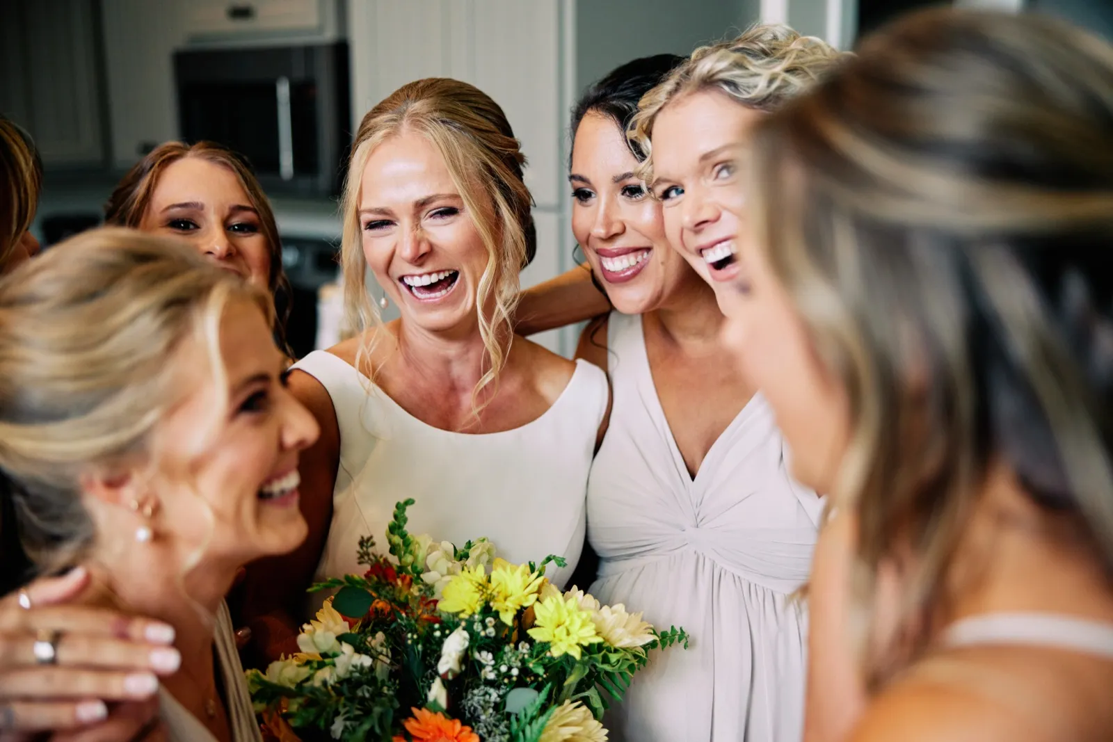 The bride laughs in the center of a tight huddle of bridesmaids holding her autumn bouquet, with two bridesmaids softly framing the foreground. — Tim Larsen Photography, Brainerd Lakes MN