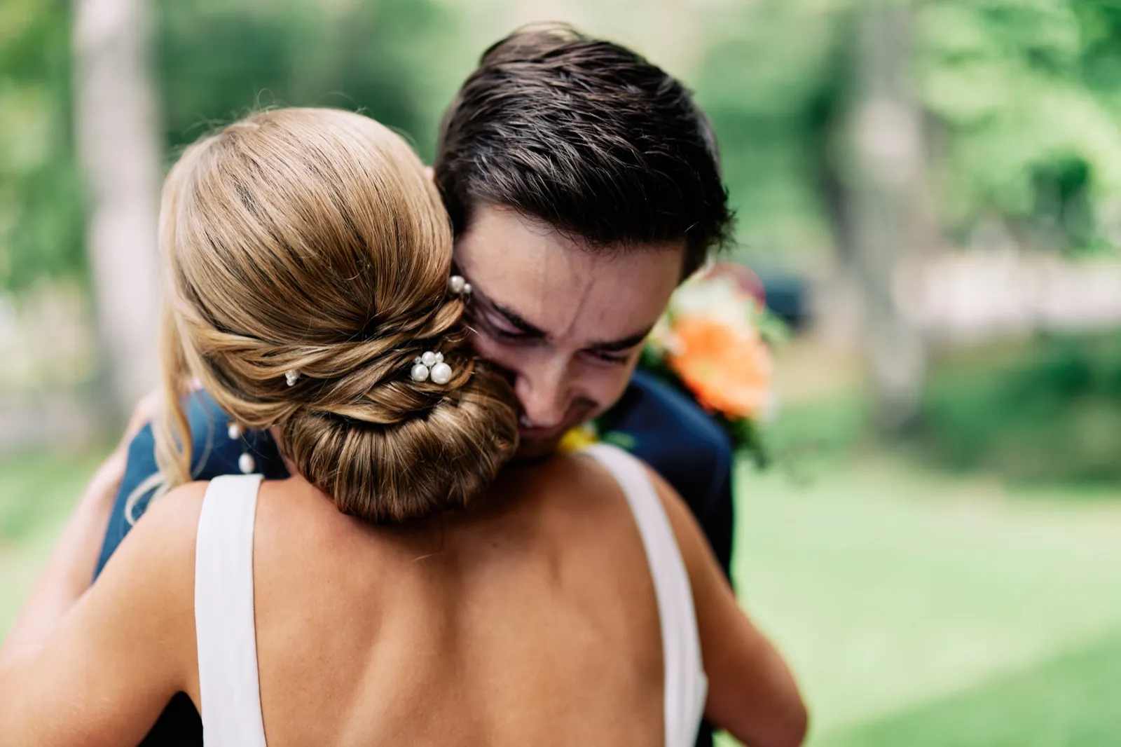 The groom's face is visible over the bride's shoulder, eyes closed in emotion, as the couple embraces tightly outdoors with her pearl-pinned updo in the foreground. — Tim Larsen Photography, Brainerd Lakes MN