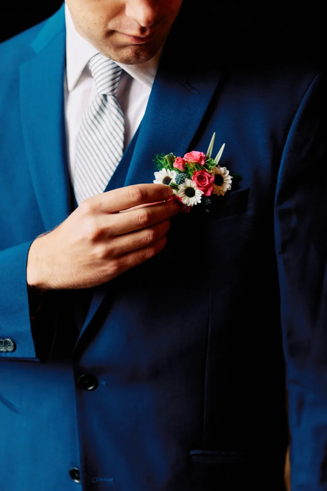 Craig adjusts the pink-and-white boutonniere on his blue suit, his striped tie visible in a close-up — Tim Larsen Photography, Brainerd Lakes MN