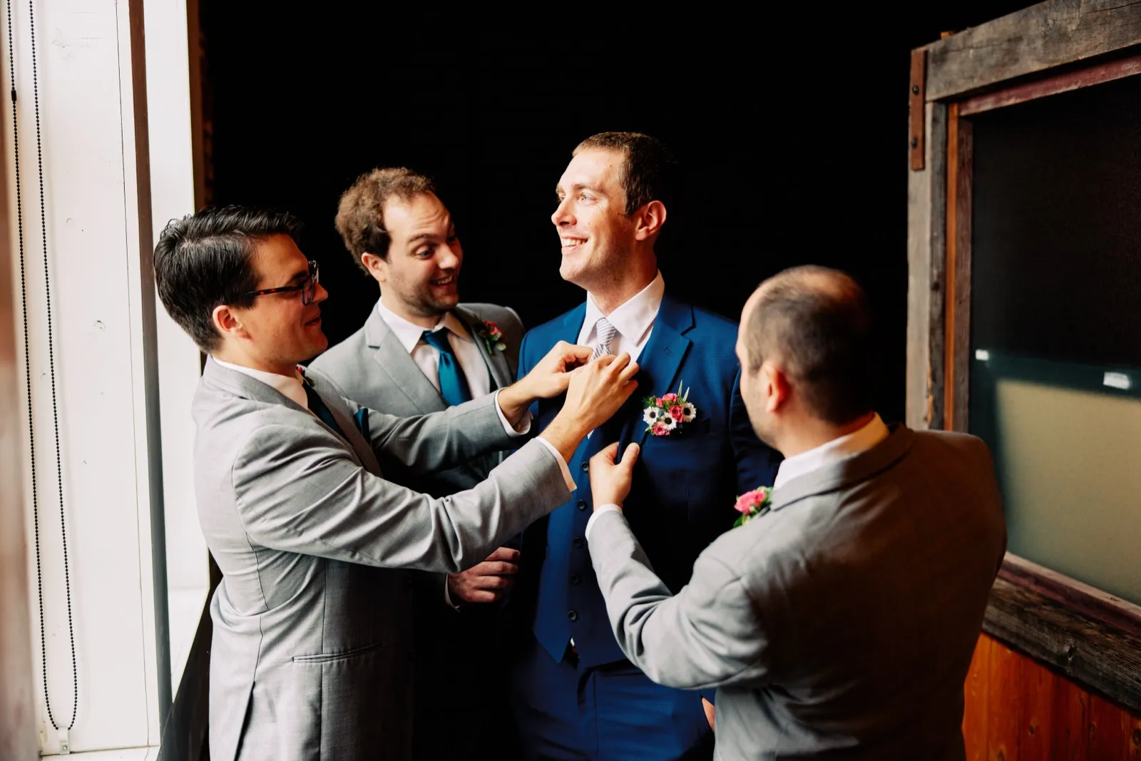Craig laughs as his groomsmen gather around to straighten his tie and boutonniere in the window light — Tim Larsen Photography, Brainerd Lakes MN