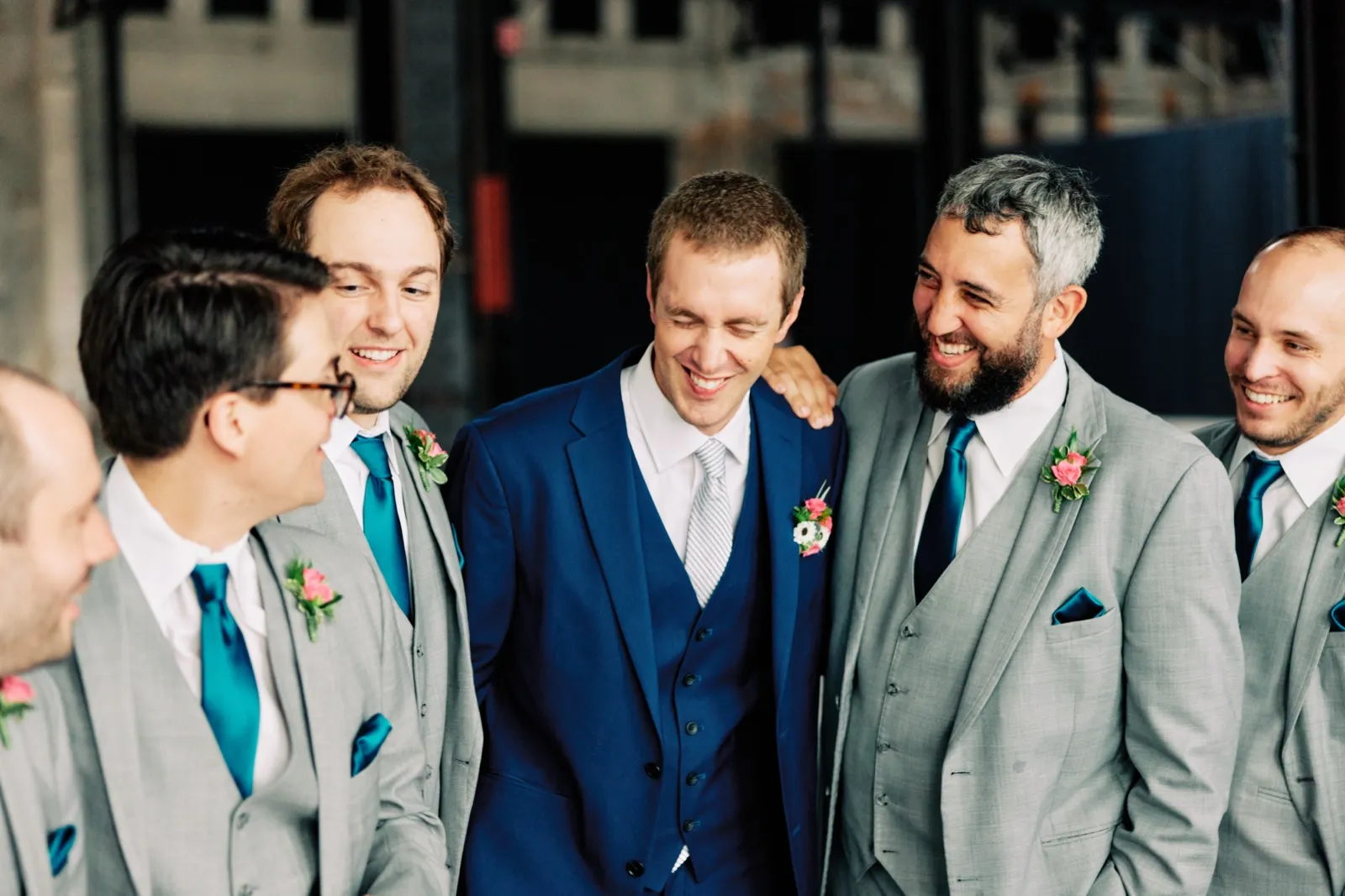 Craig looks down laughing as his groomsmen in gray suits and teal ties crowd around him inside Northern Pacific Center — Tim Larsen Photography, Brainerd Lakes MN