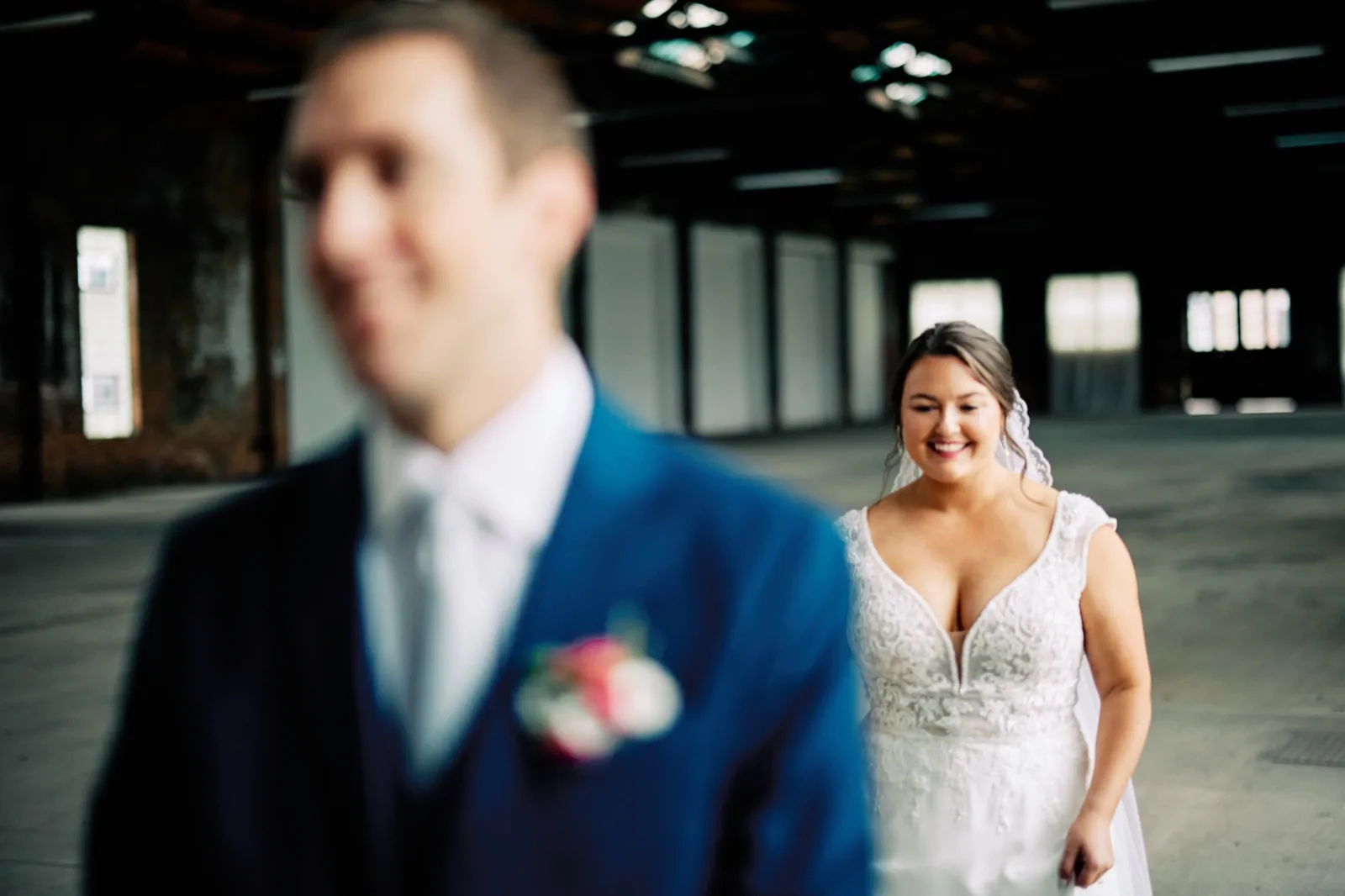 Maggie smiles as she approaches Craig from behind for their first look, his blue suit softly out of focus in the foreground — Tim Larsen Photography, Brainerd Lakes MN