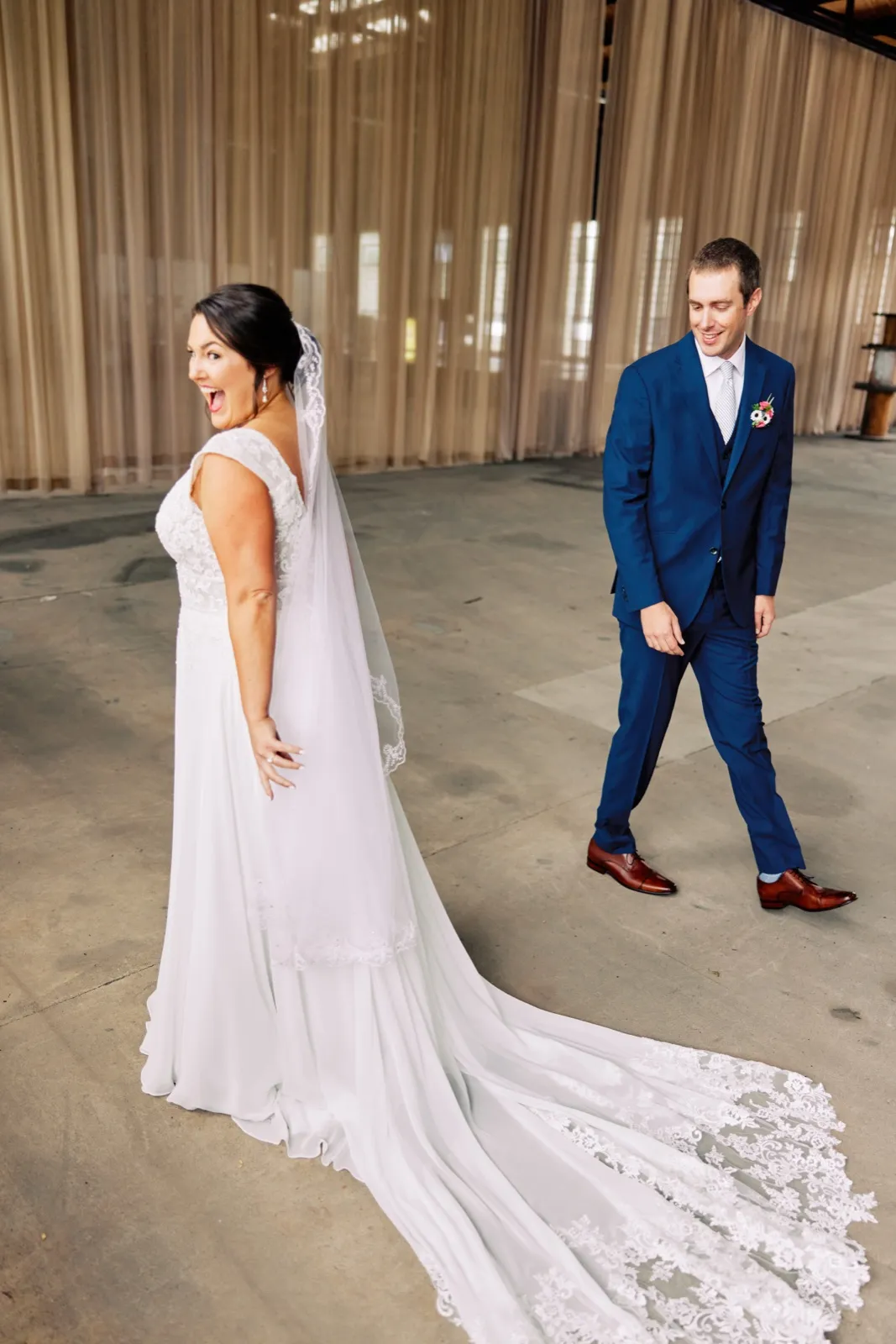 Maggie looks back smiling as Craig turns toward her during their first look, her lace train trailing across the concrete floor — Tim Larsen Photography, Brainerd Lakes MN
