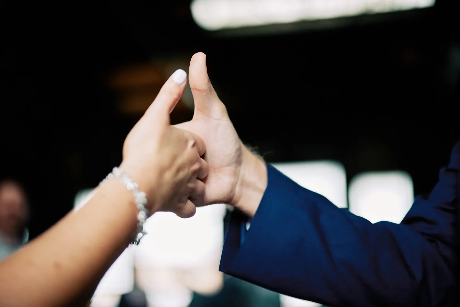 Maggie and Craig touch their raised thumbs together in a playful close-up against the dark warehouse interior — Tim Larsen Photography, Brainerd Lakes MN