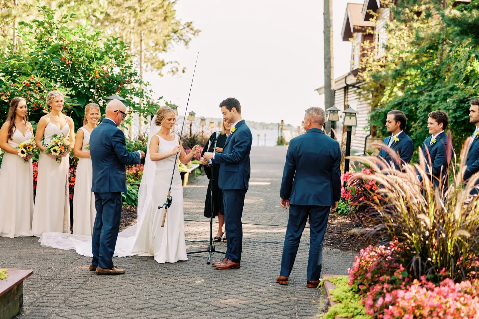 The bride and groom hold a fishing rod together during their outdoor lakeside ceremony at Grand View Lodge while the bridal party and officiant look on. — Tim Larsen Photography, Brainerd Lakes MN