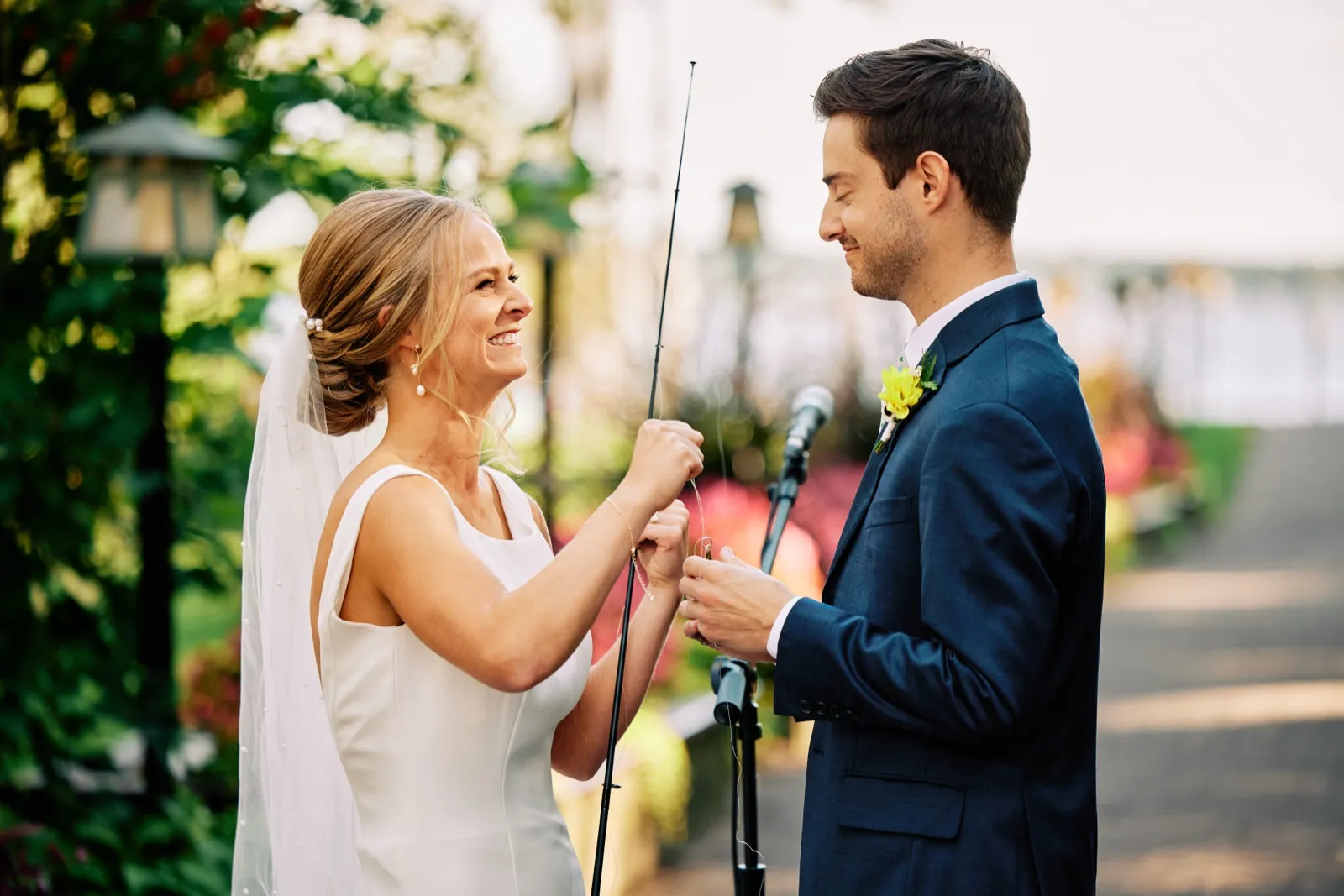 The bride laughs as she and the groom hold a fishing rod between them during their outdoor lakeside ceremony. — Tim Larsen Photography, Brainerd Lakes MN