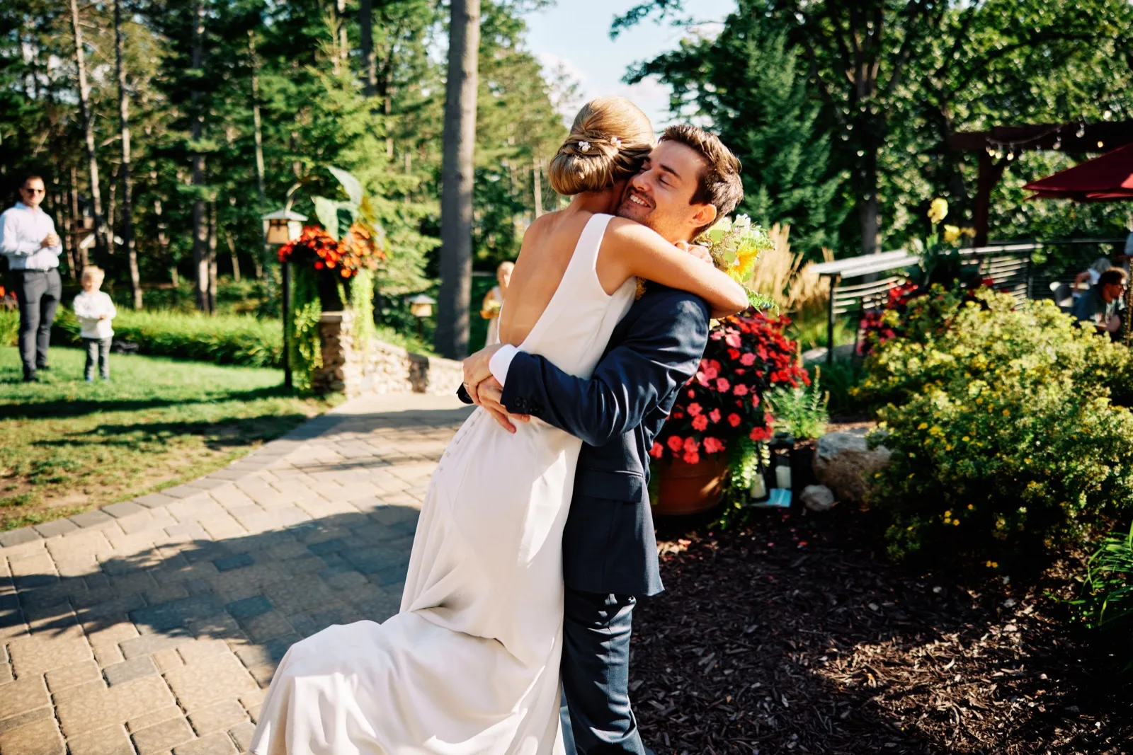 The groom lifts the bride off the ground in an embrace on a stone garden path at Grand View Lodge, surrounded by flowering planters and trees. — Tim Larsen Photography, Brainerd Lakes MN
