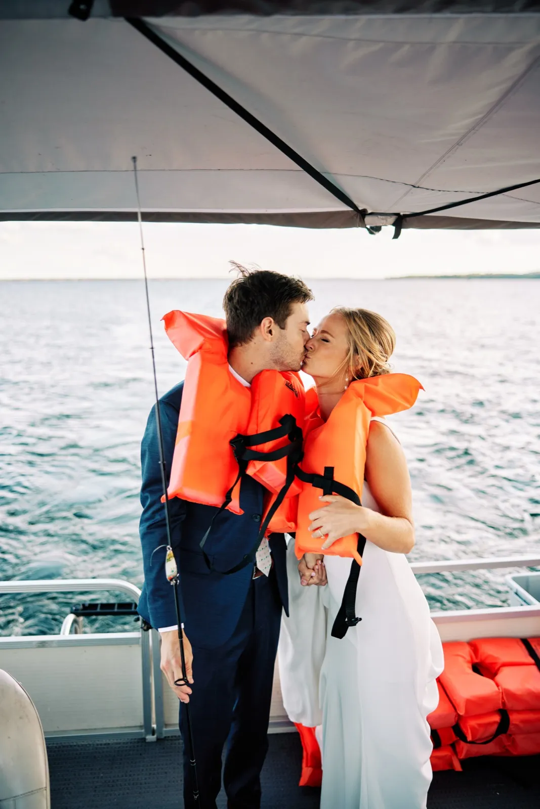 The bride and groom kiss on a pontoon boat on Gull Lake while wearing bright orange life vests over their wedding attire.