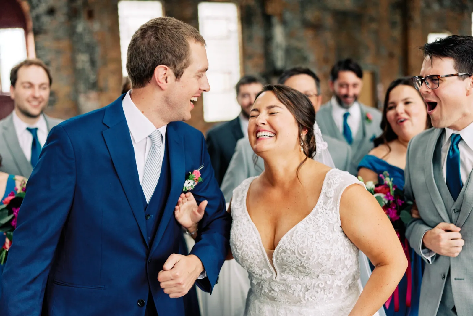 Maggie and Craig laugh together as their wedding party gathers close around them inside the brick hall — Tim Larsen Photography, Brainerd Lakes MN
