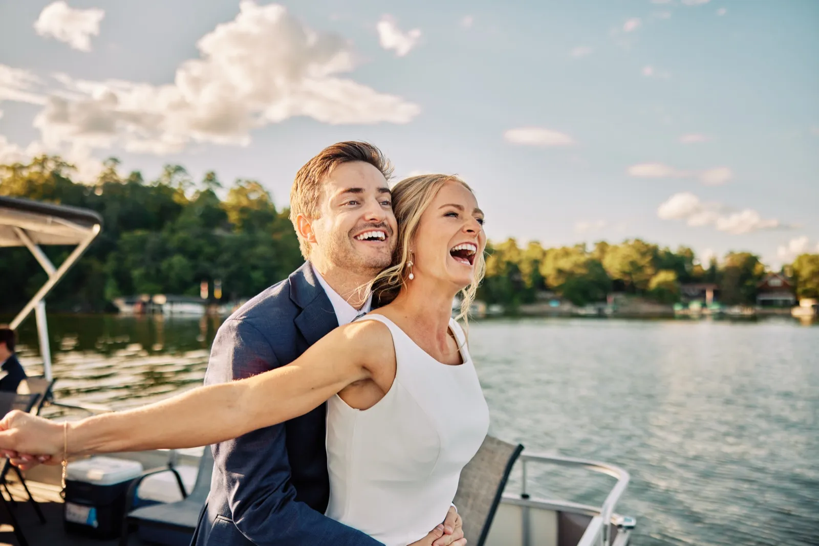 The bride and groom laugh openly while standing on a pontoon boat at golden hour with Gull Lake stretching behind them. — Tim Larsen Photography, Brainerd Lakes MN