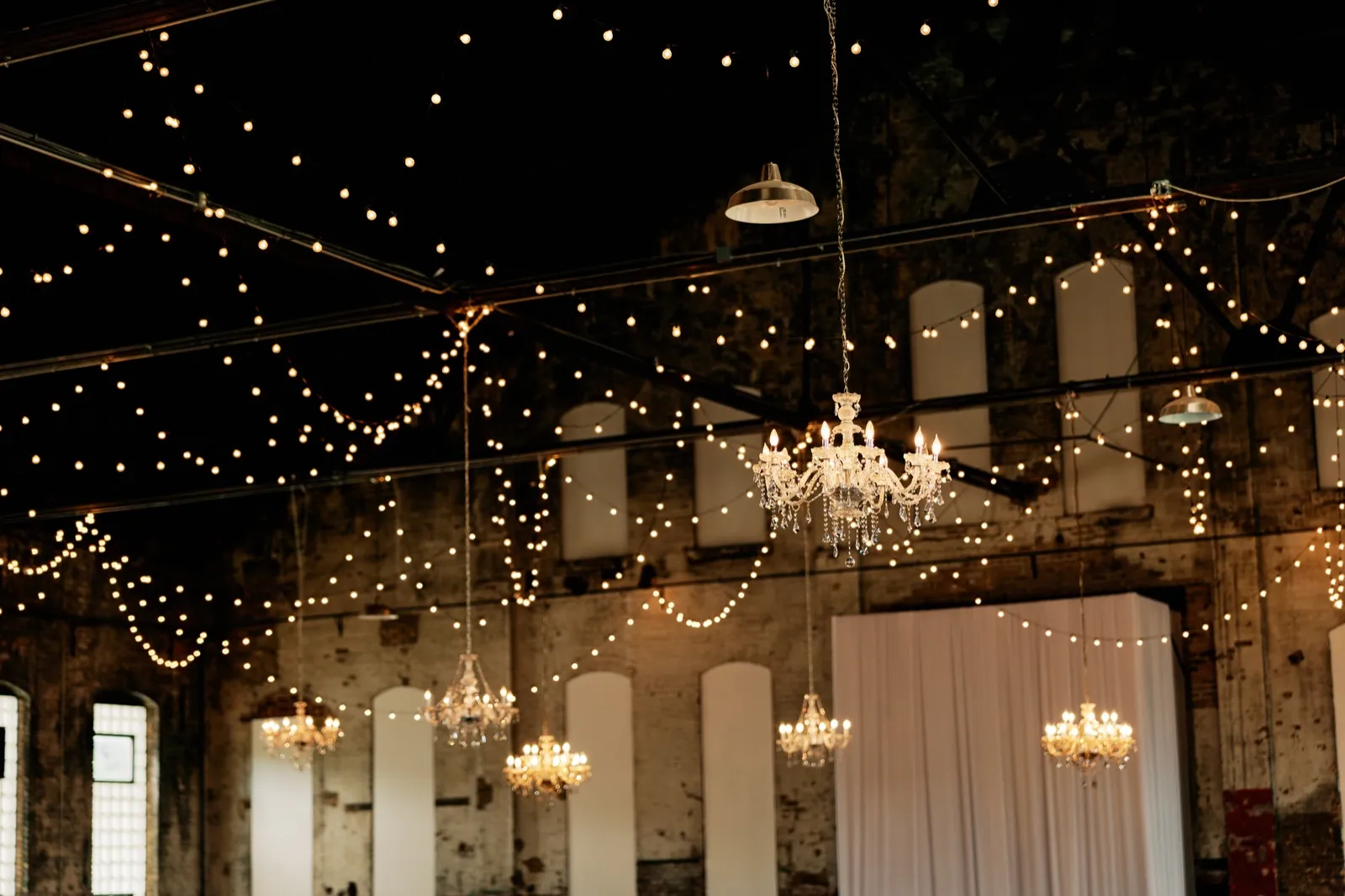 Crystal chandeliers and strings of bistro lights hang above Maggie and Craig's reception space at Northern Pacific Center — Tim Larsen Photography, Brainerd Lakes MN