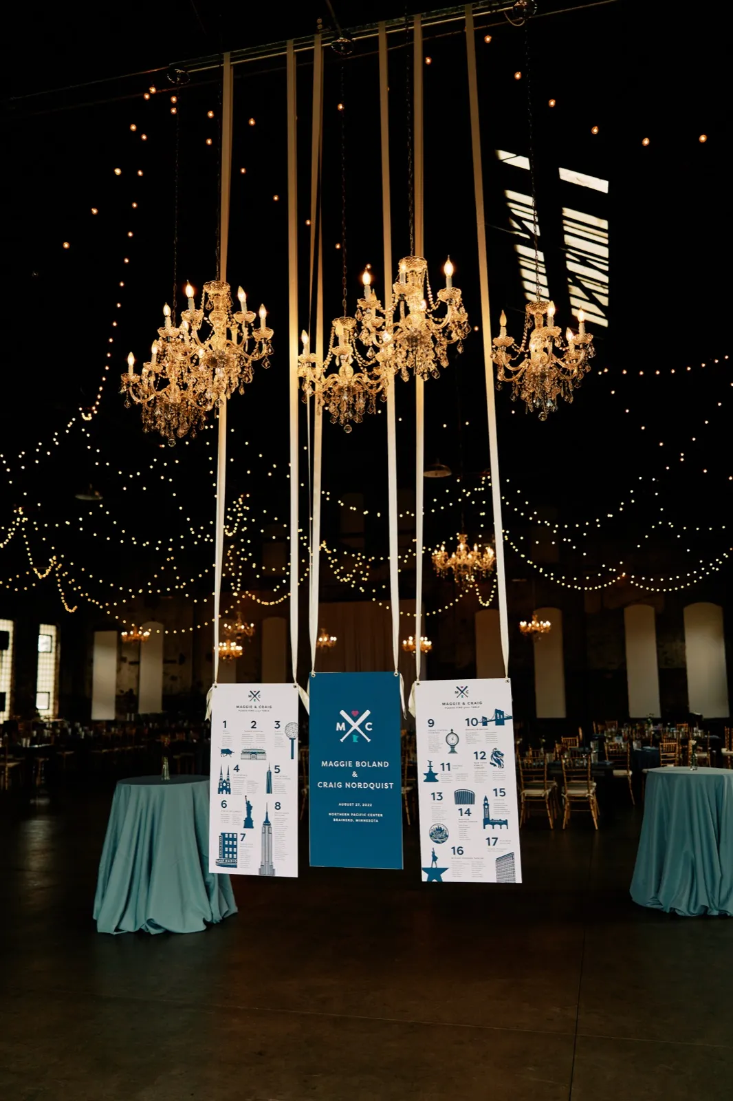 Maggie and Craig's three seating-chart banners hang beneath crystal chandeliers and strings of lights in the reception hall — Tim Larsen Photography, Brainerd Lakes MN