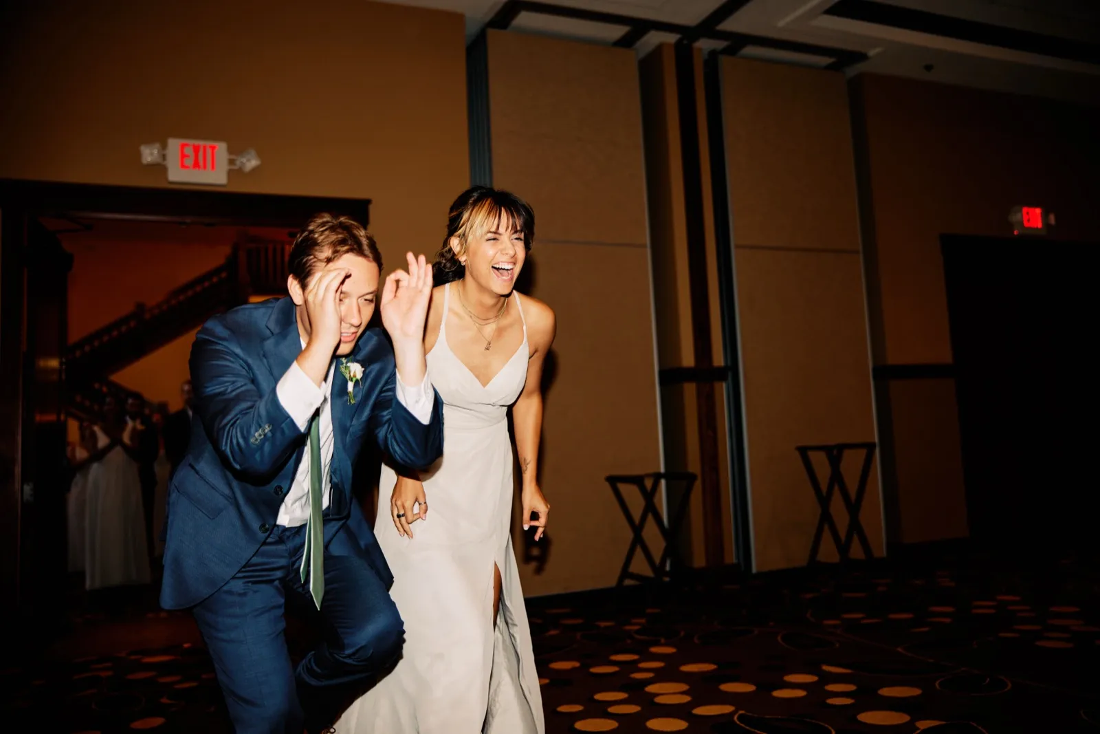 The bride laughs and waves while the groom bashfully covers his face as the couple makes their grand entrance into the reception ballroom. — Tim Larsen Photography, Brainerd Lakes MN